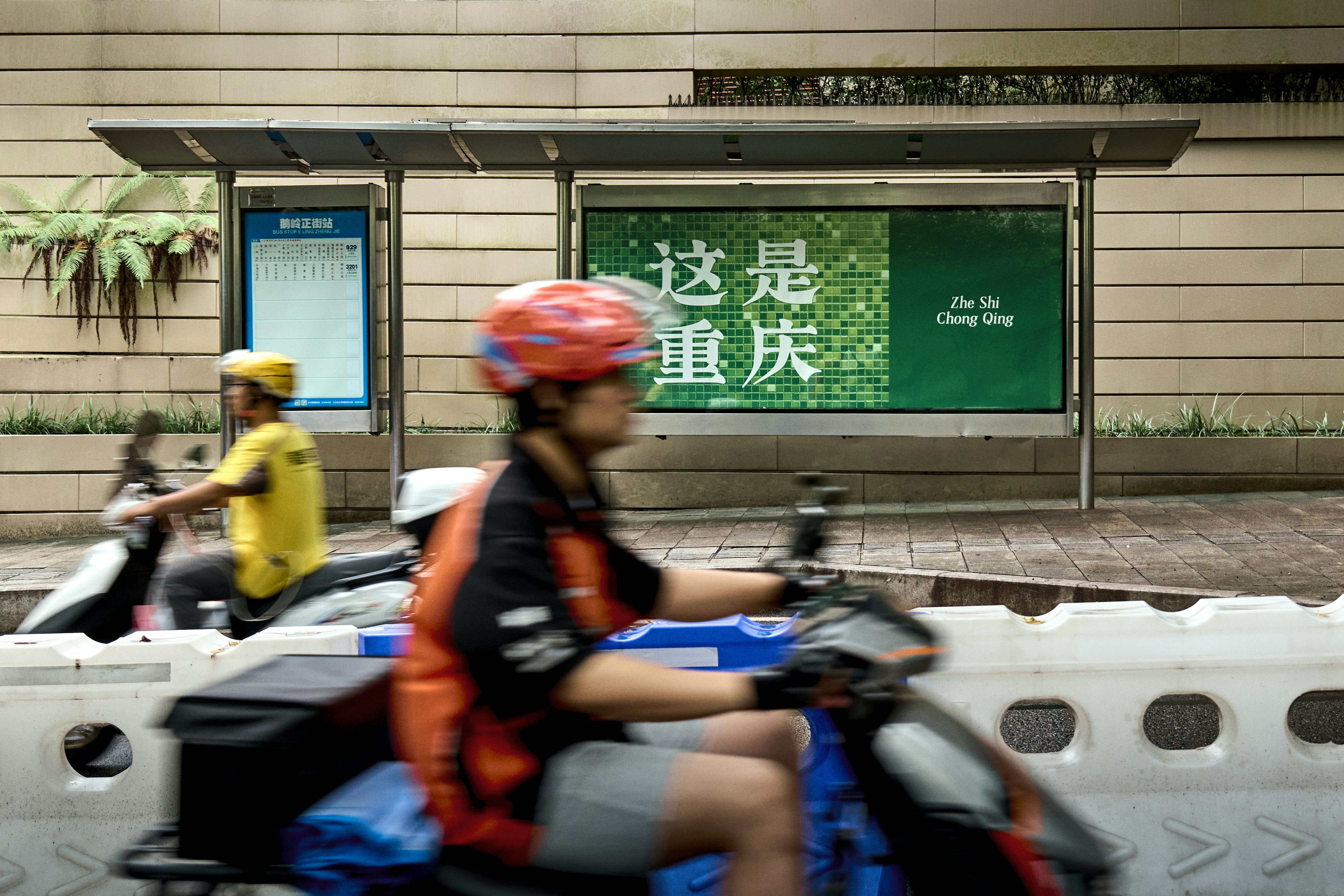 Entregadores com desfoque de movimento em scooters passam por um outdoor verde.