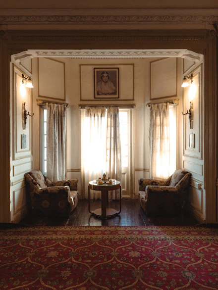 Elegant sitting area with armchairs, table, and sunlit windows.