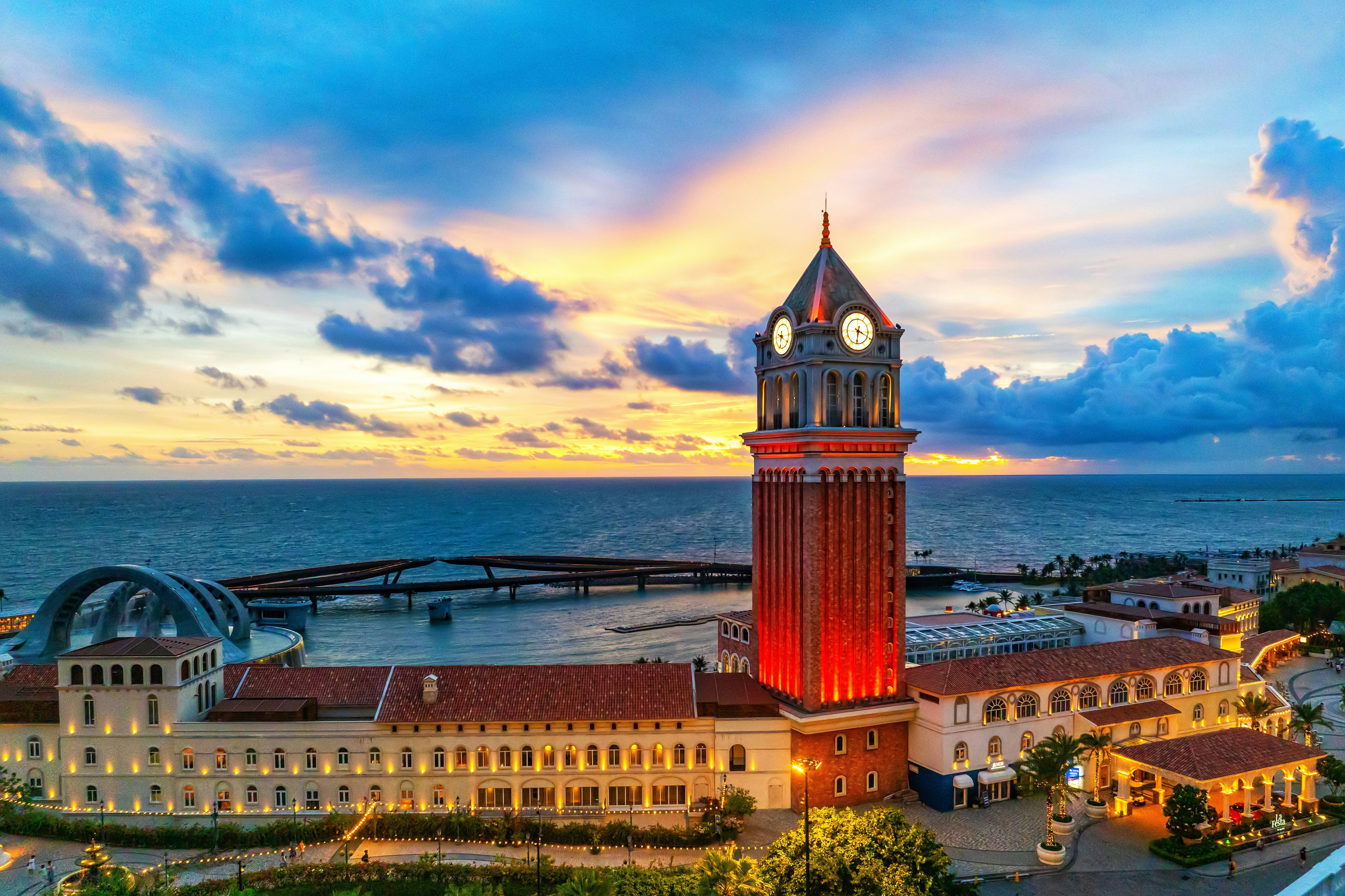 Ein hoher Uhrturm steht am Meer bei Sonnenuntergang.