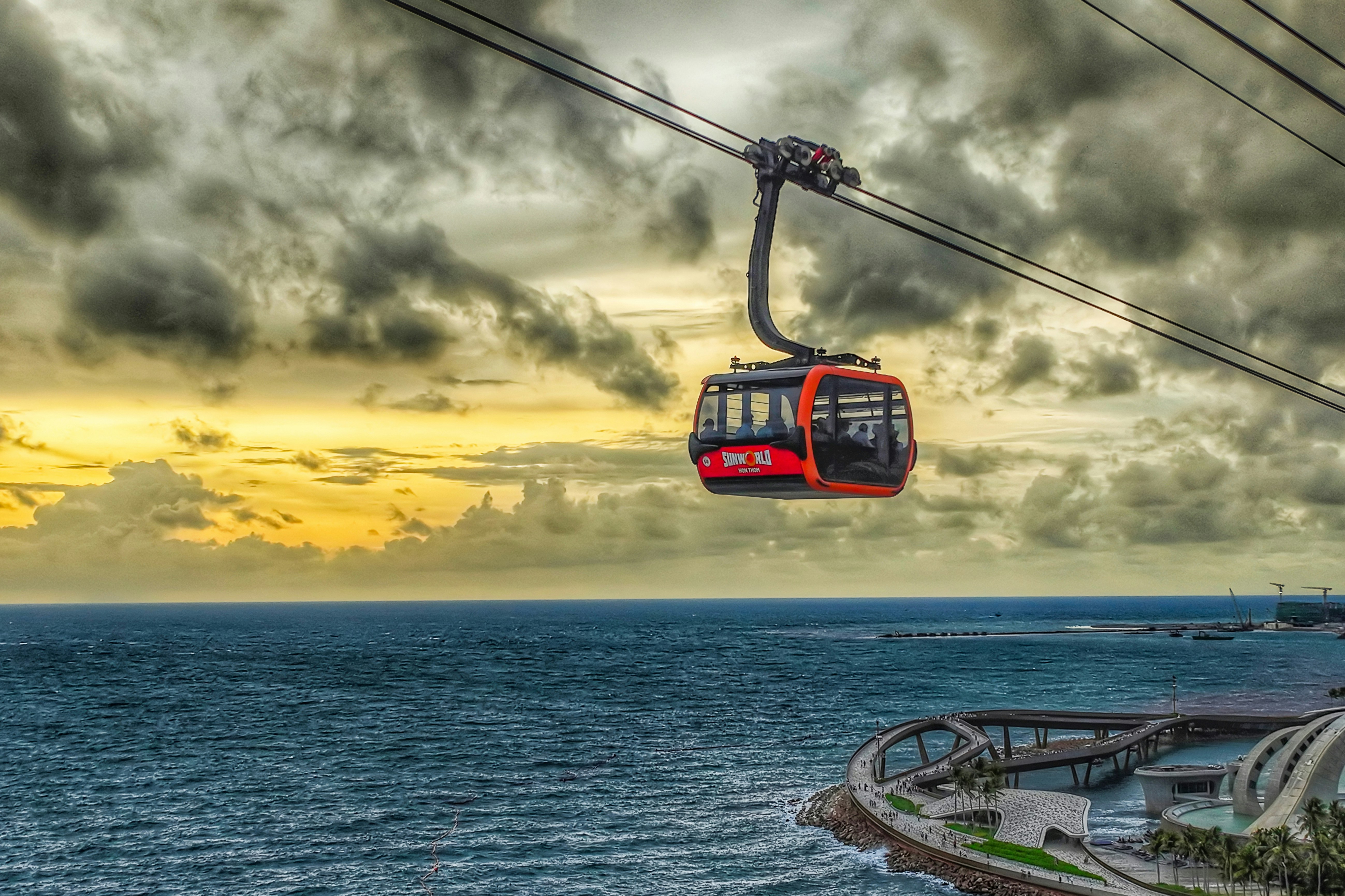 Eine rote Seilbahn fährt bei Sonnenuntergang über den Ozean.
