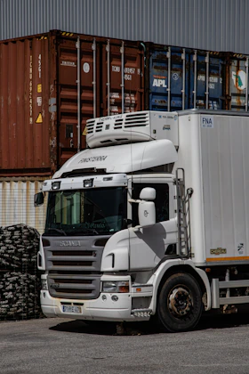 A white semi-truck parked in front of shipping containers.