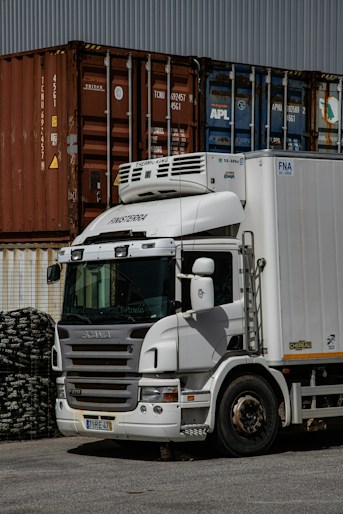Biała ciężarówka chłodnicza przy kontenerach — cold chain logistics