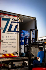 Forklift loading large blue rolls into a ferramacho transport truck