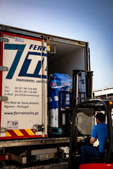 Forklift loading large blue rolls into a ferramacho transport truck