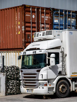 A white truck with shipping containers and stacked wood.