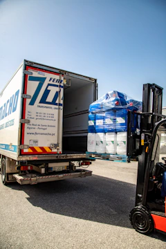Forklift loading blue and white containers into a delivery truck