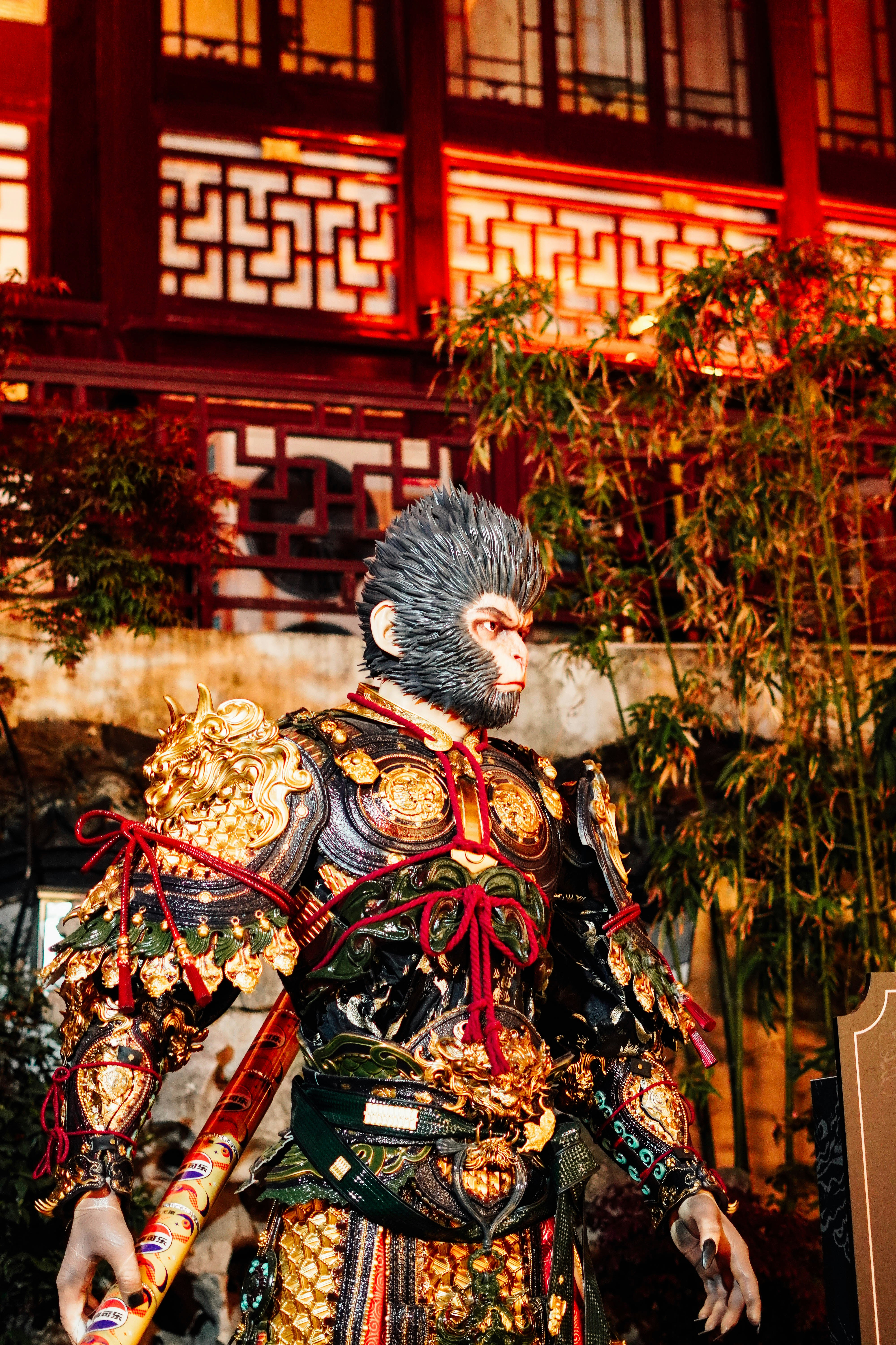 Patung raja kera dengan baju besi berornamen di depan bangunan tradisional.