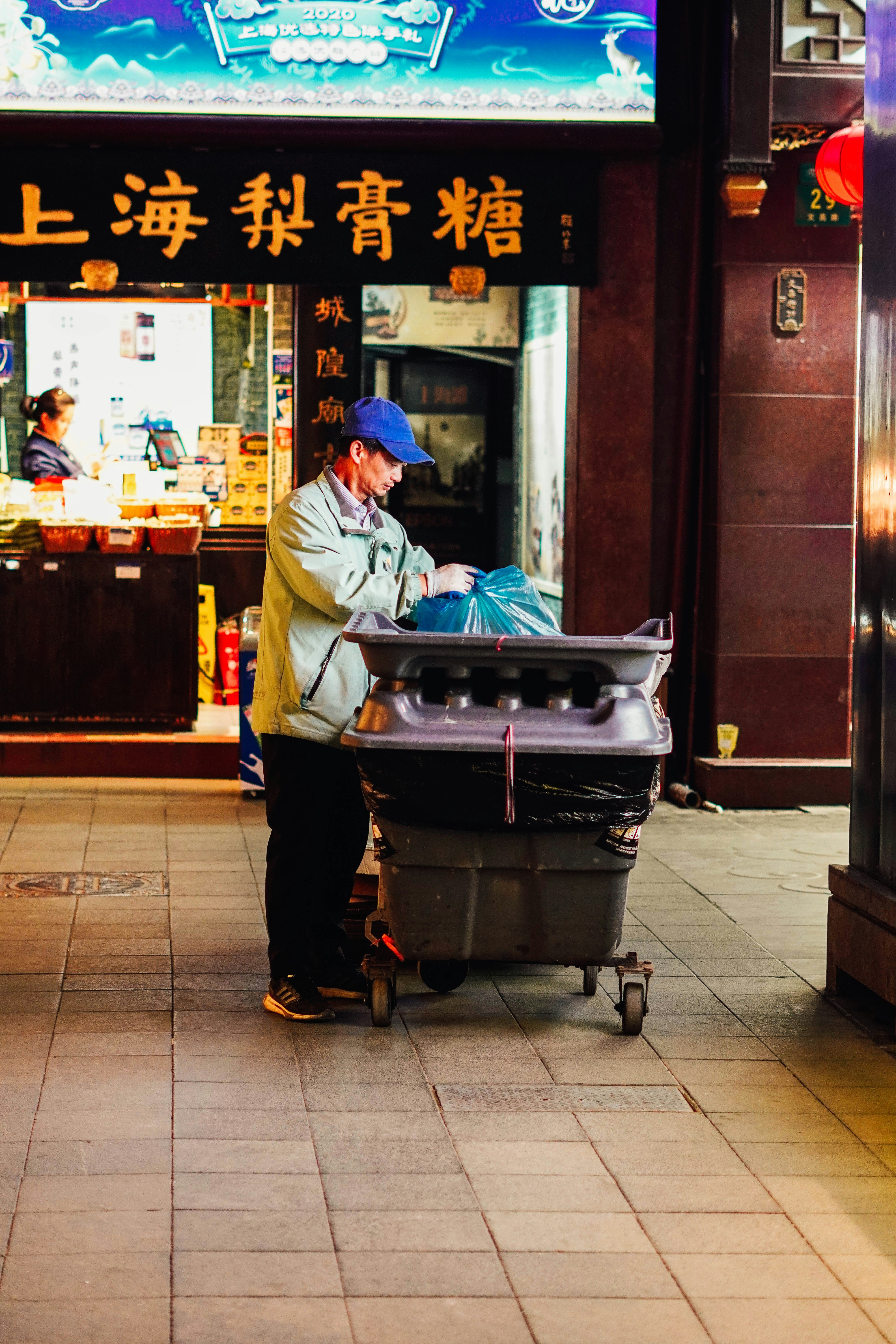 Street worker in blue cap handles a cart.