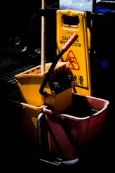 A yellow mop bucket, mop, and "caution wet floor" sign