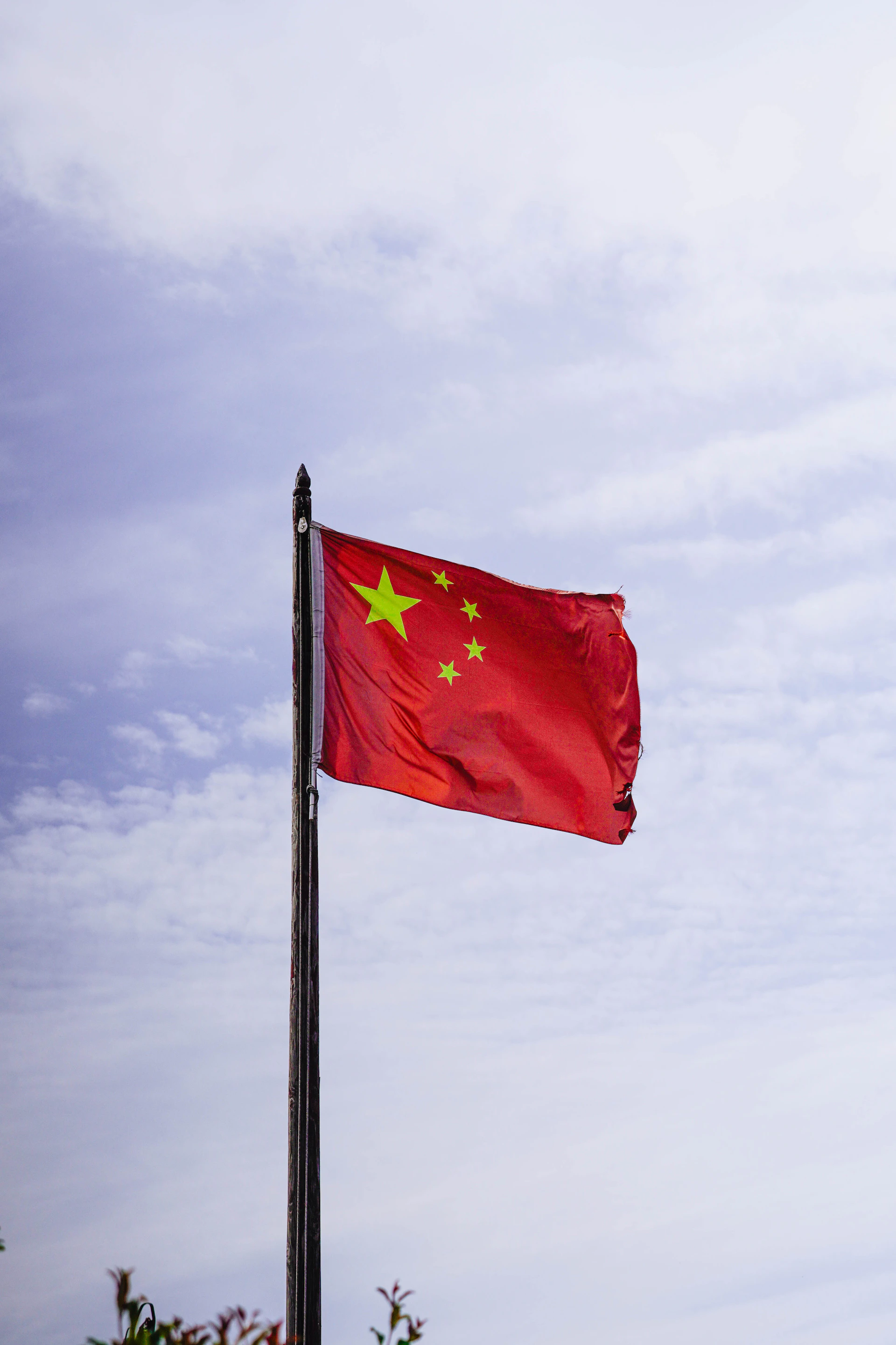Chinese flag waving on a flagpole against a cloudy sky