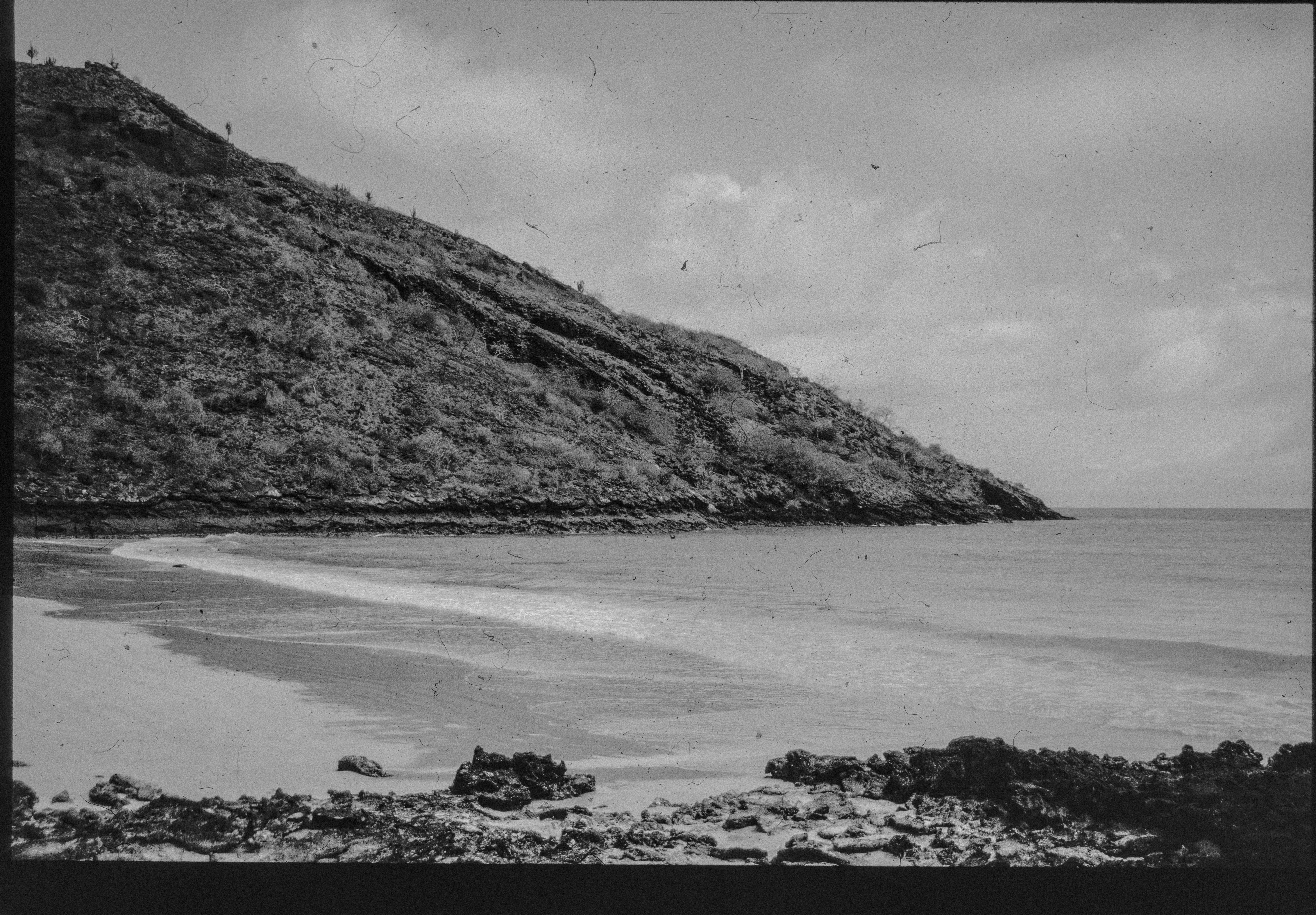 Hill slopes to calm bay with sandy beach.