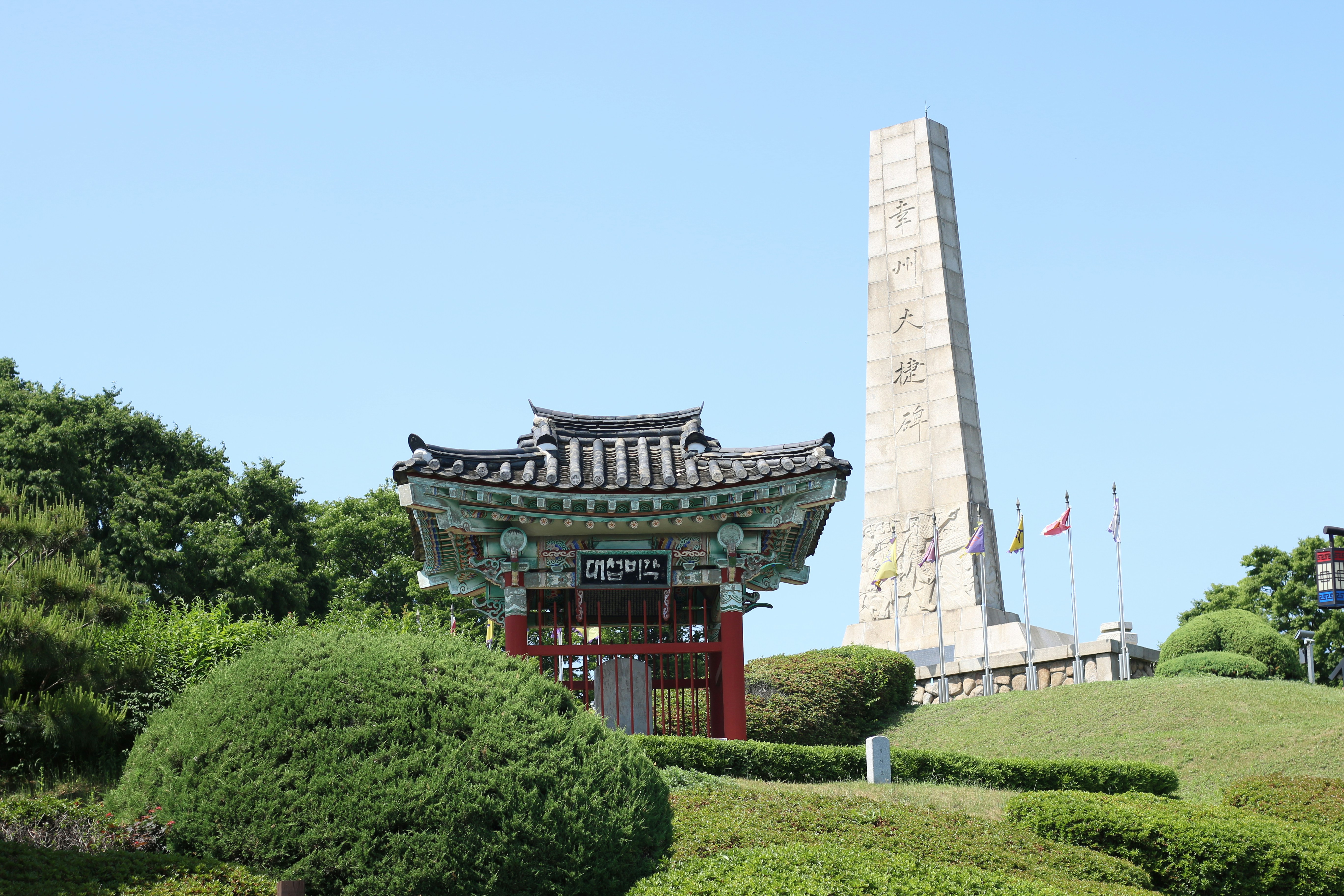Traditional korean pavilion and stone monument on a grassy hill