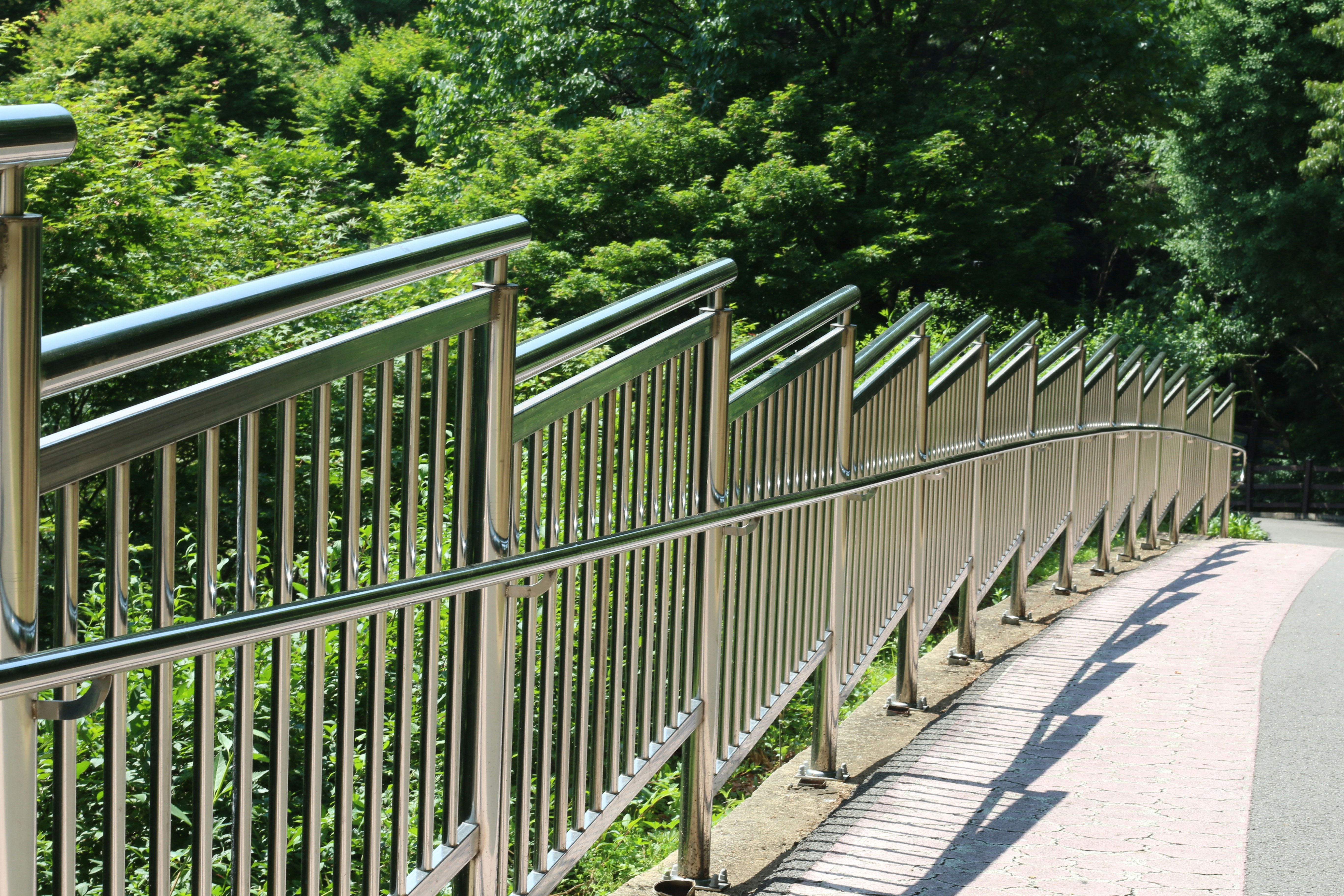 A curving metal railing alongside a path with green trees