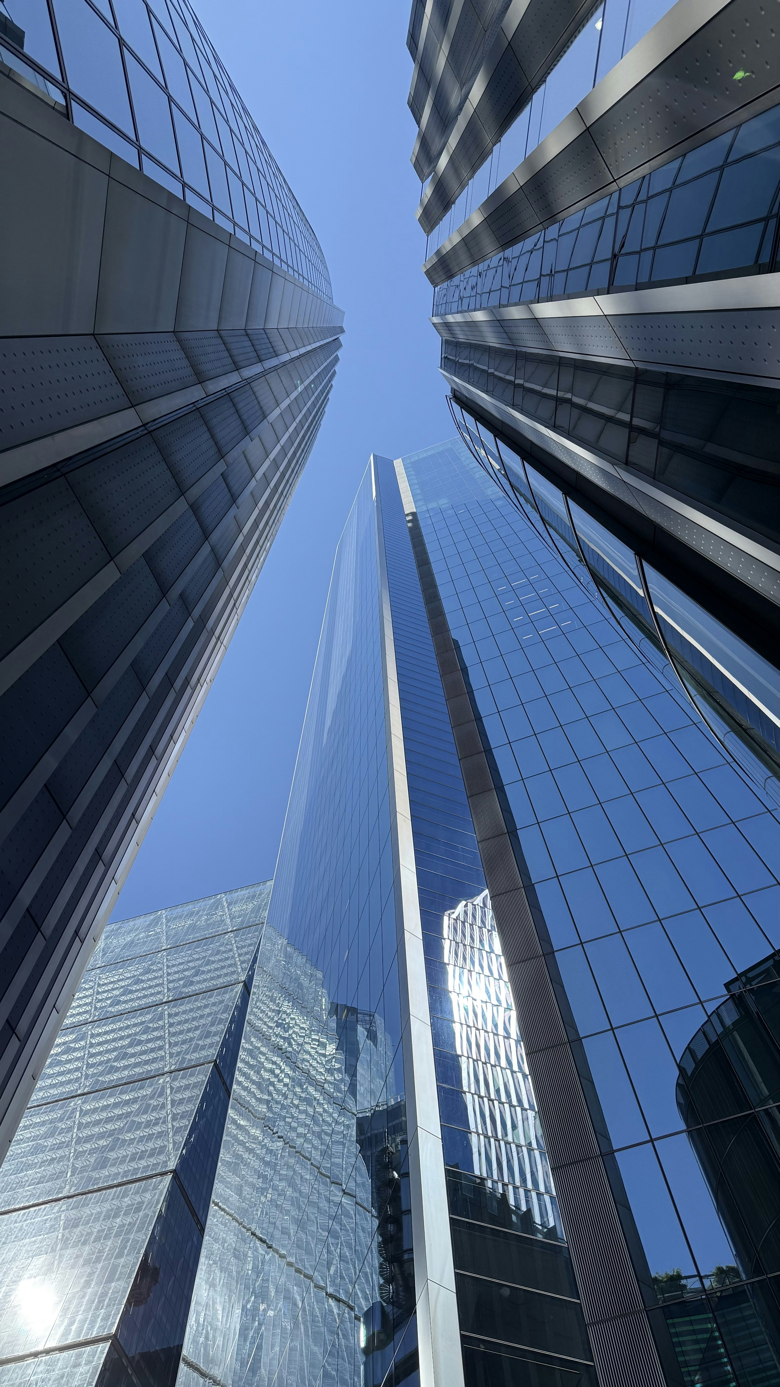 Tall glass skyscrapers reflecting blue sky and surrounding buildings