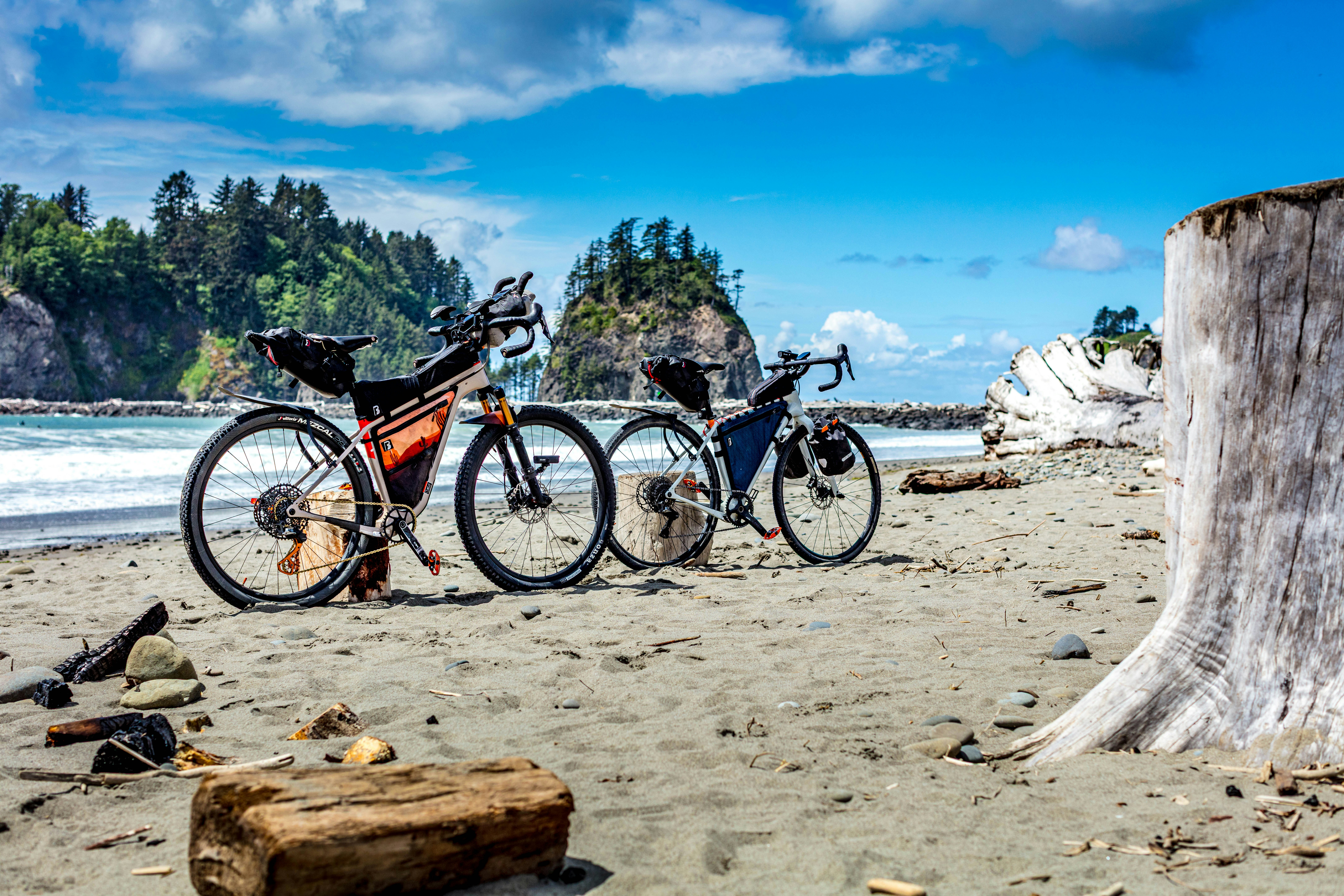 Two bicycles parked on a sandy beach by the ocean.