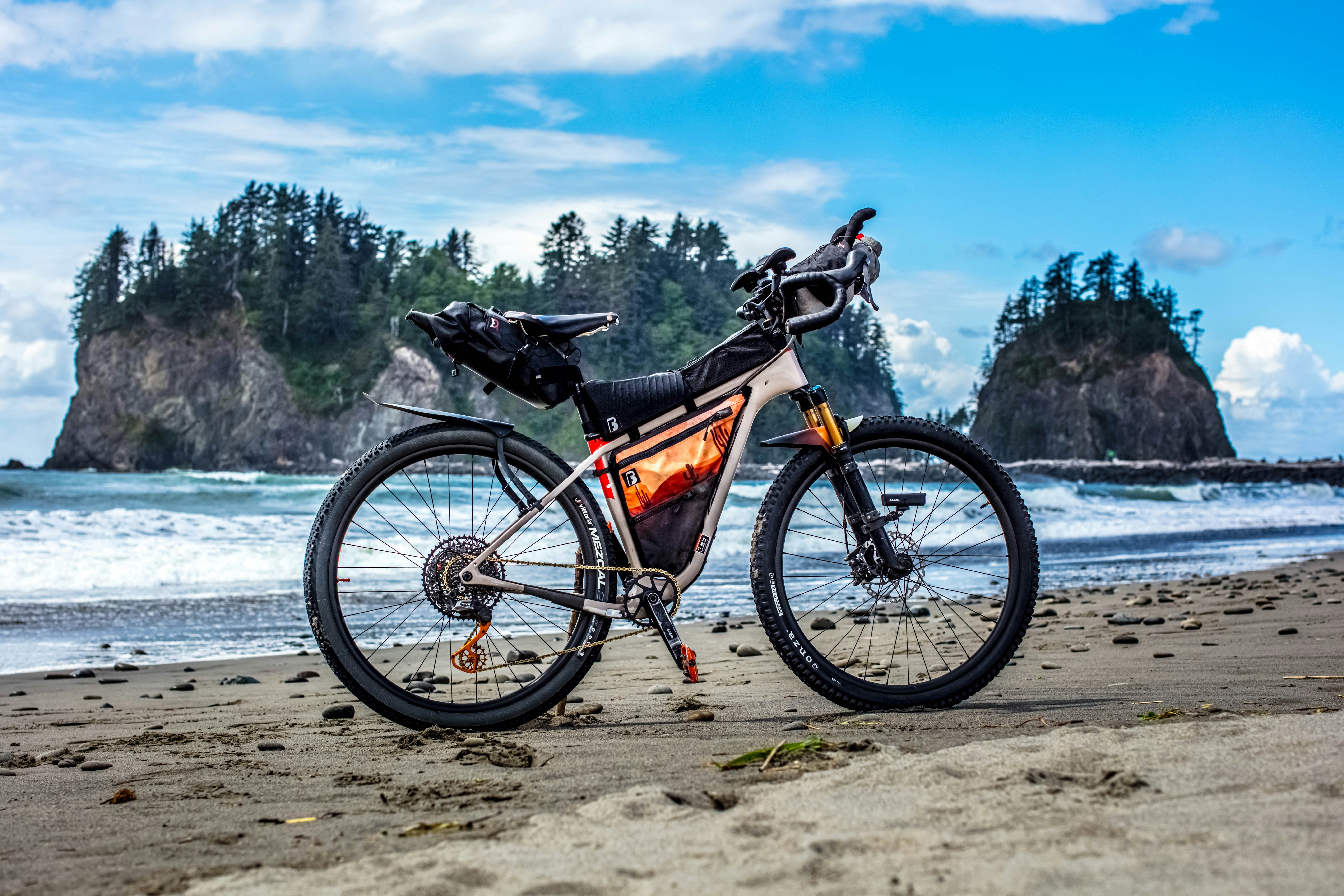 A bicycle parked on a sandy beach with sea stacks.