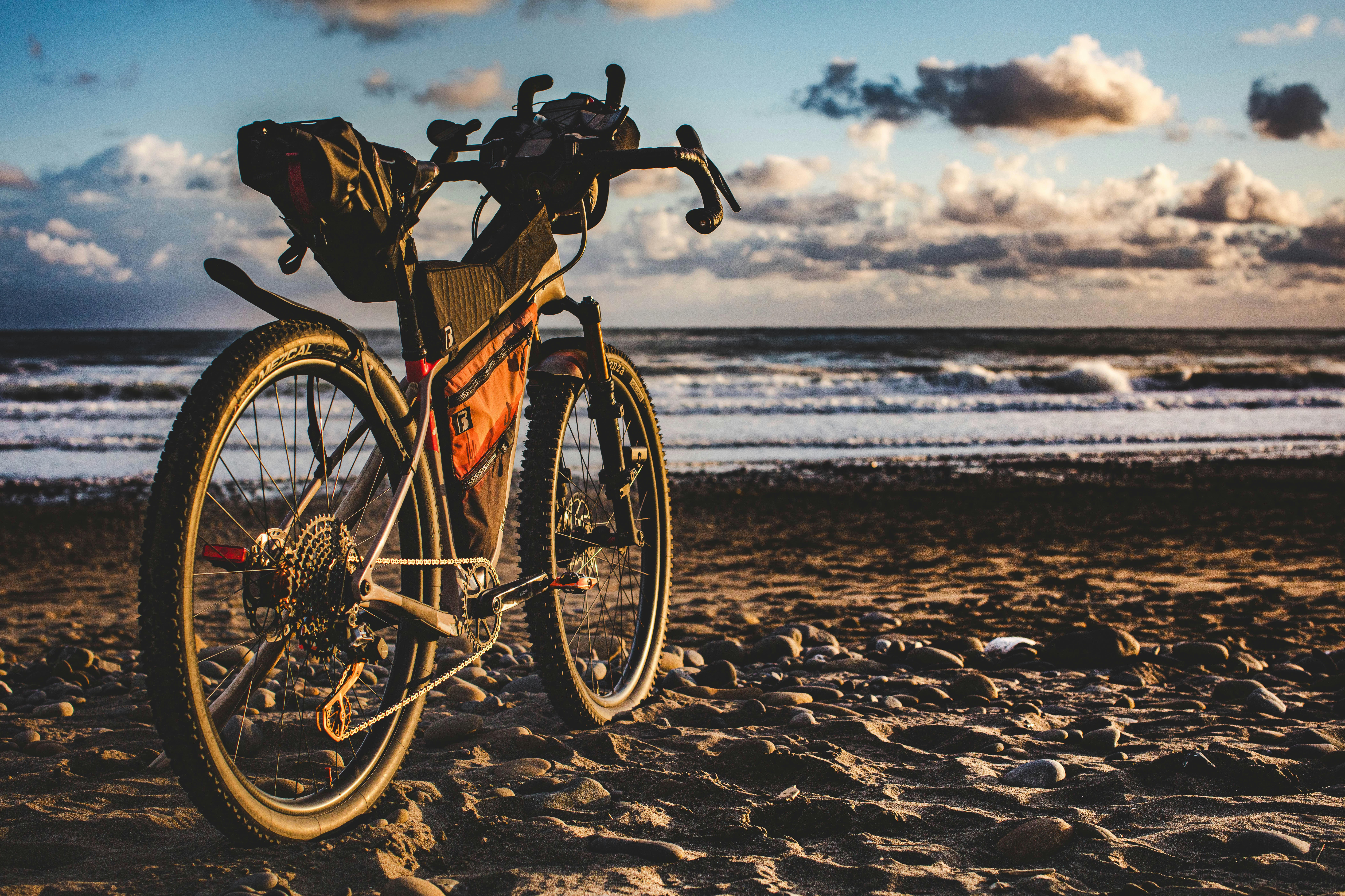 Bicycle resting on a sandy beach beside the ocean.