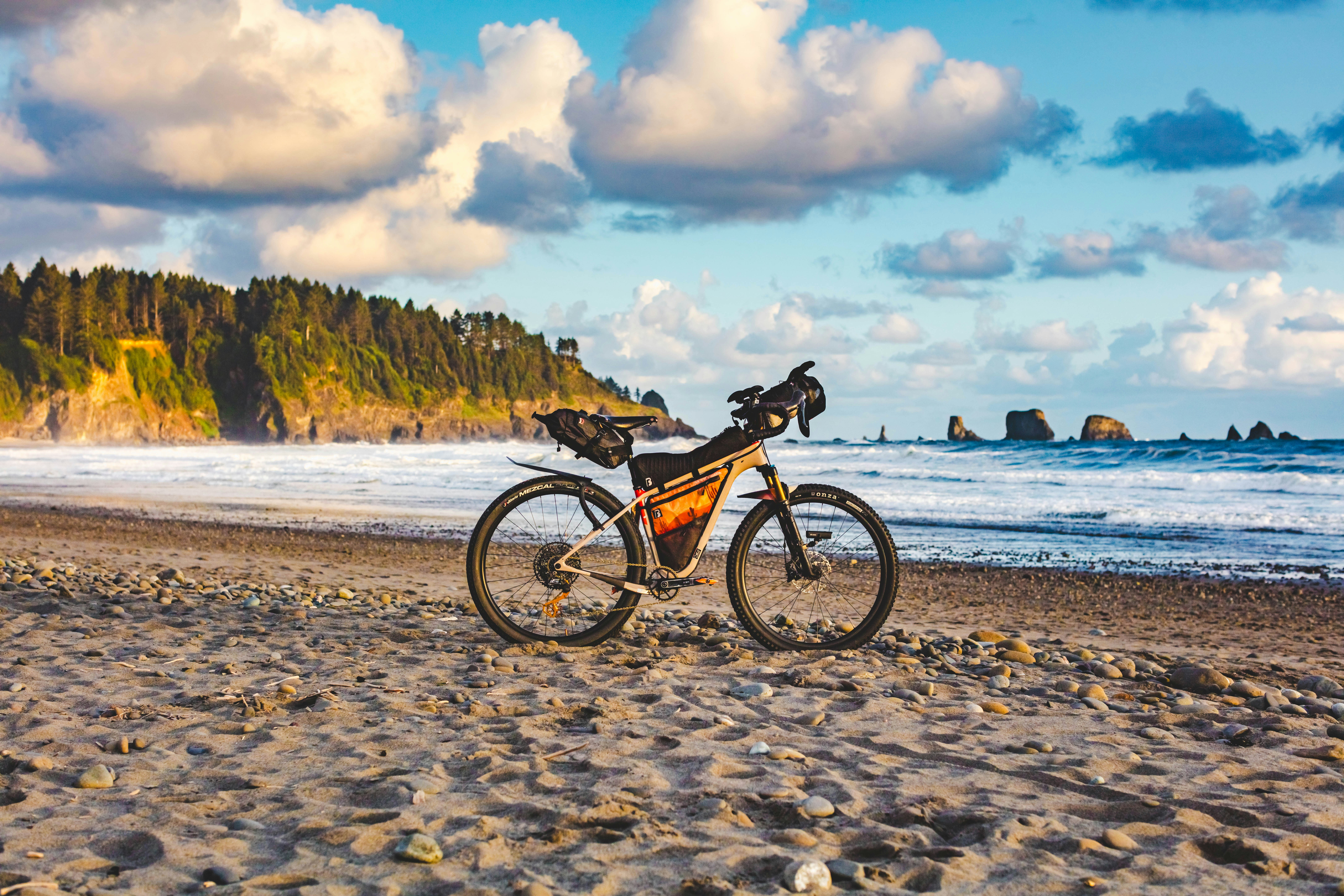 Bicycle parked on a sandy beach with ocean and cliffs.
