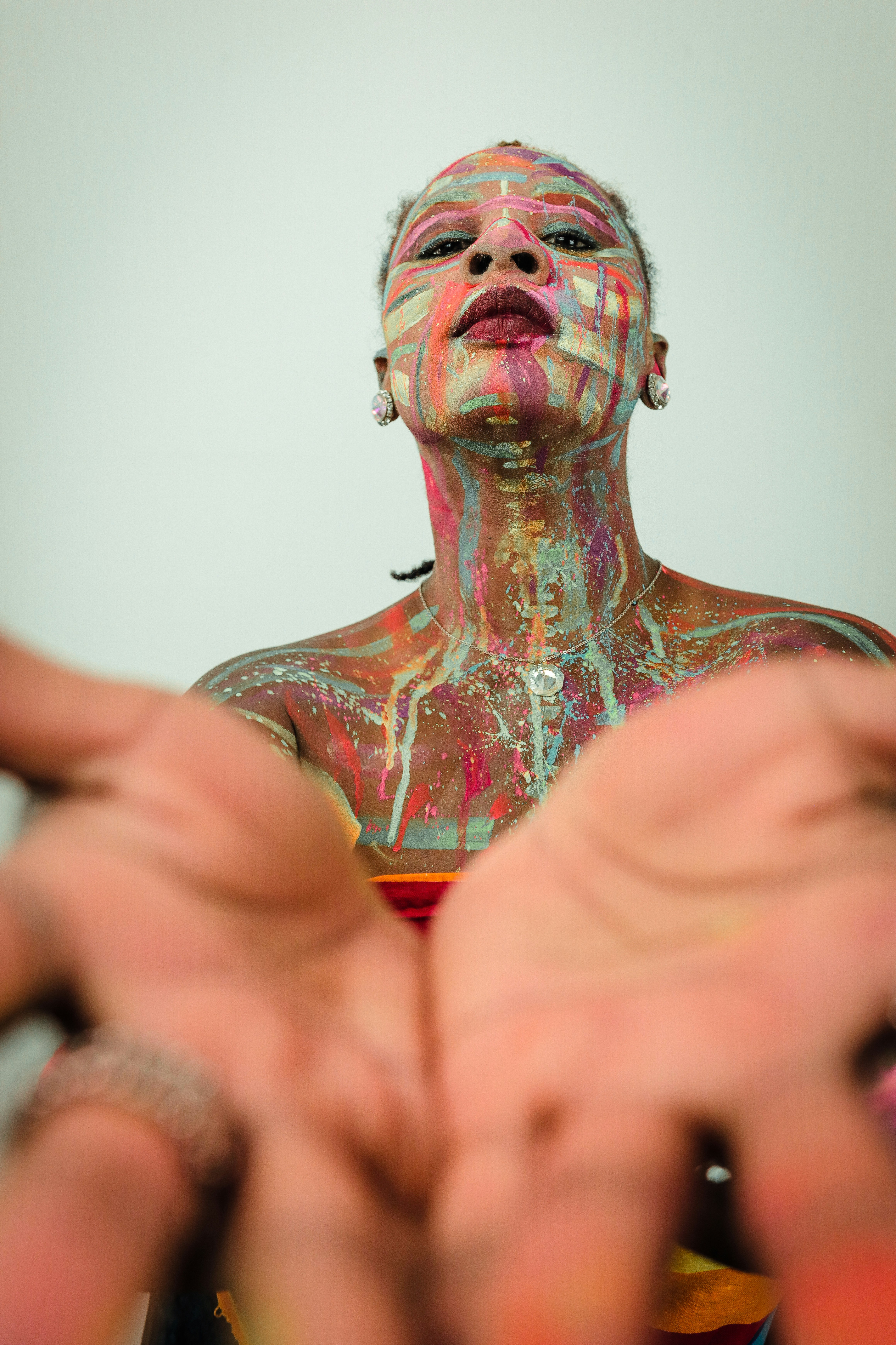 A person covered in colorful dripping paint with outstretched hands.