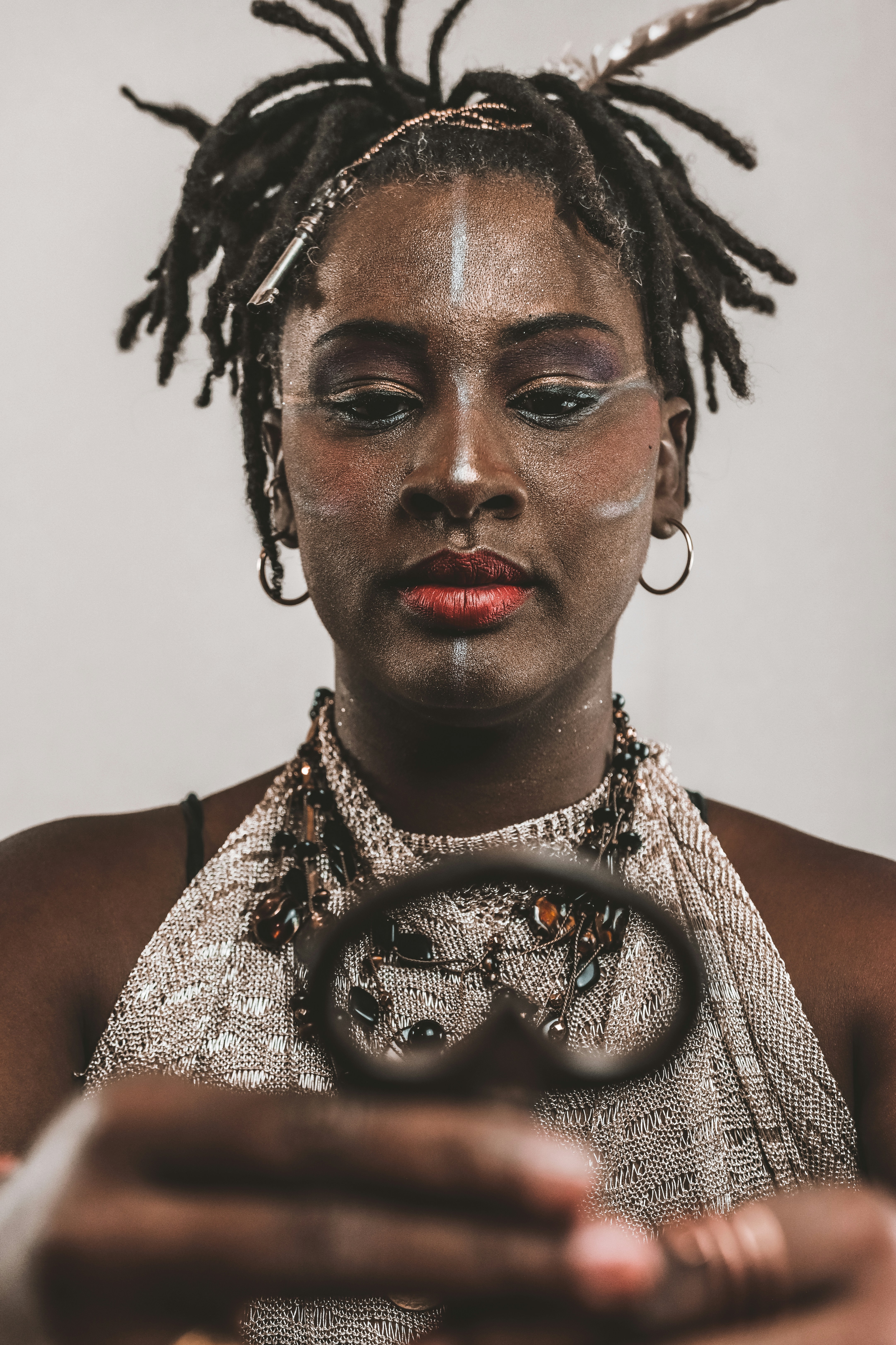 Woman with face paint and dreadlocks examining a decorative object.