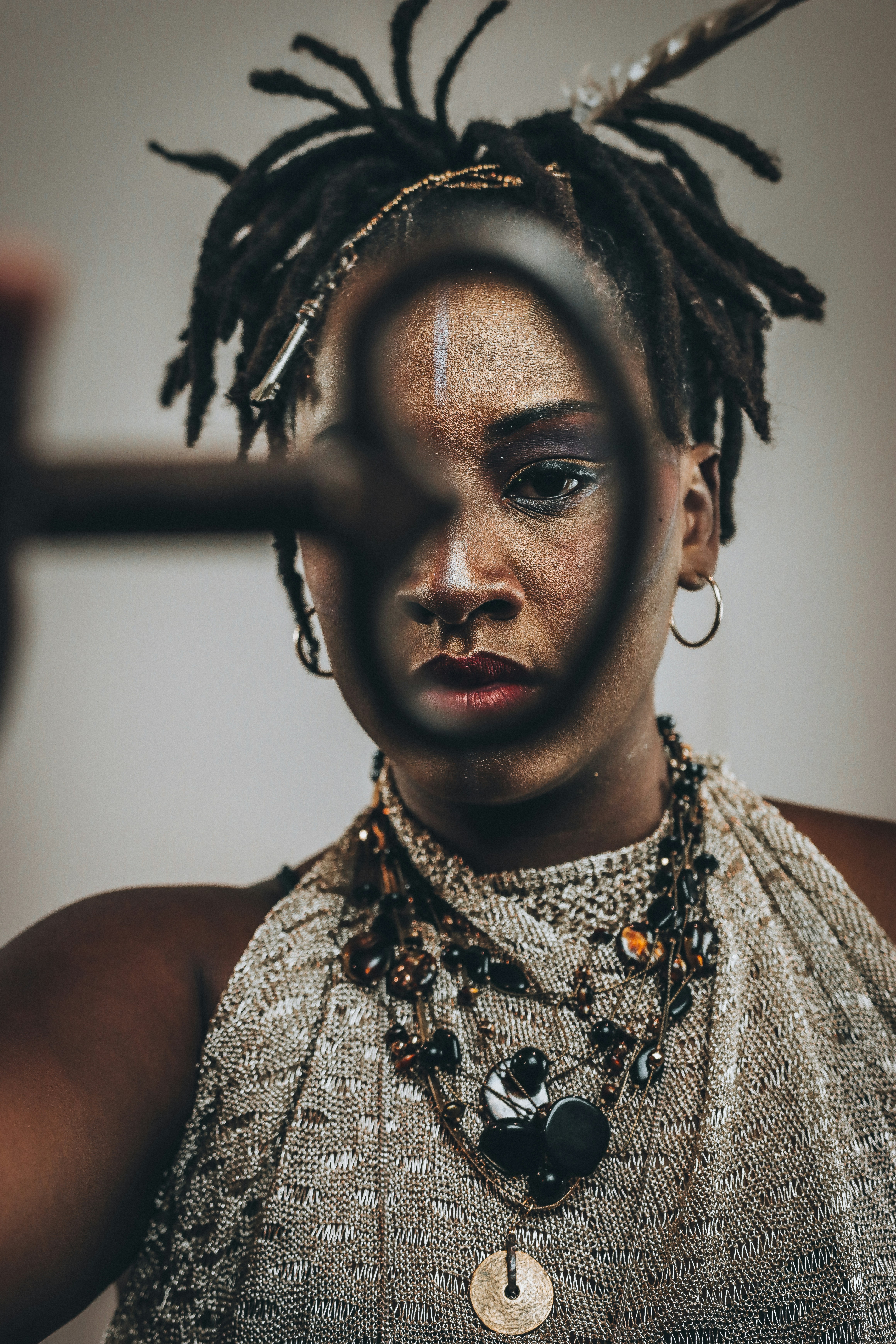 Woman with dreadlocks and makeup looks through a magnifying glass.