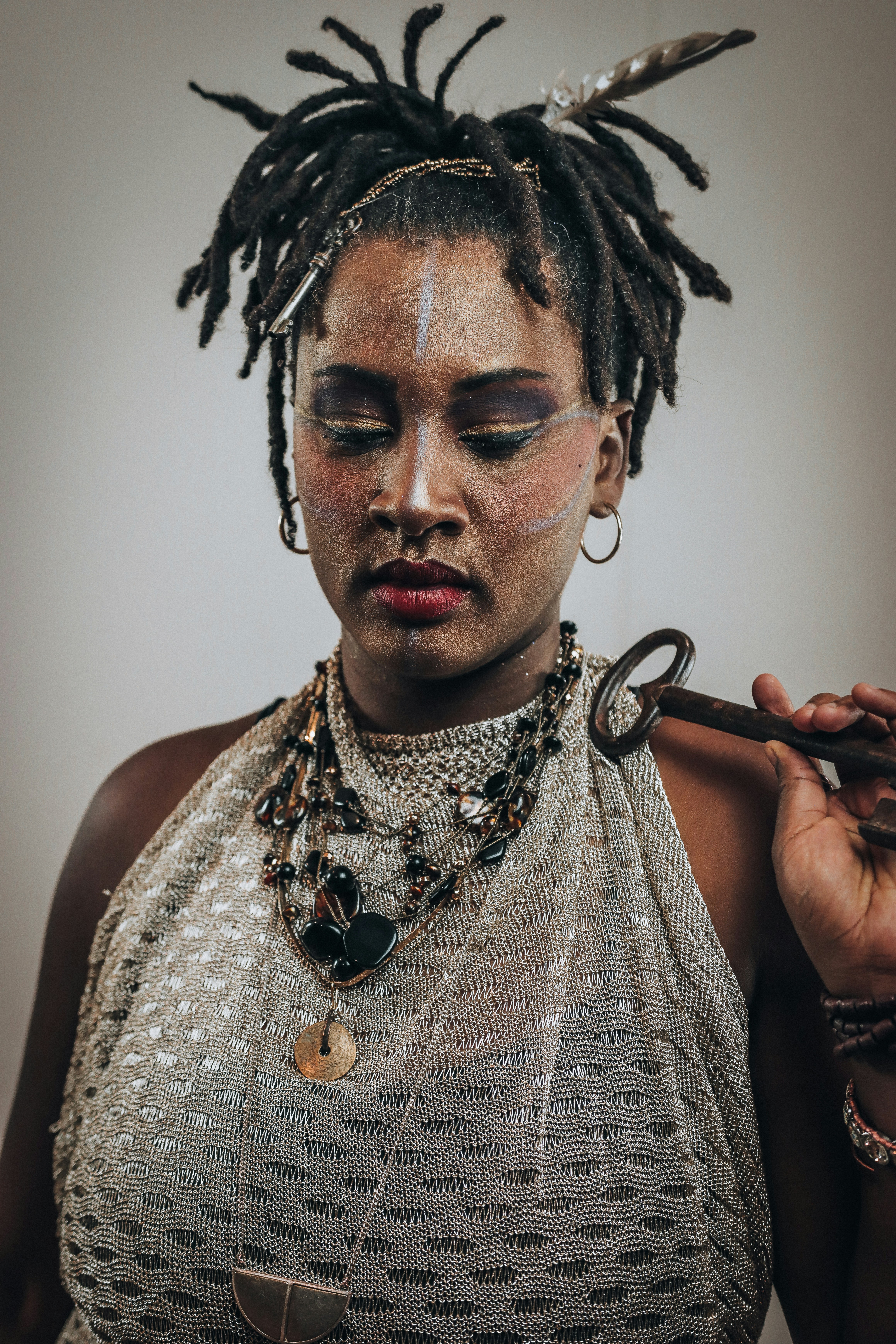 A woman with dreadlocks and makeup holds an antique key.