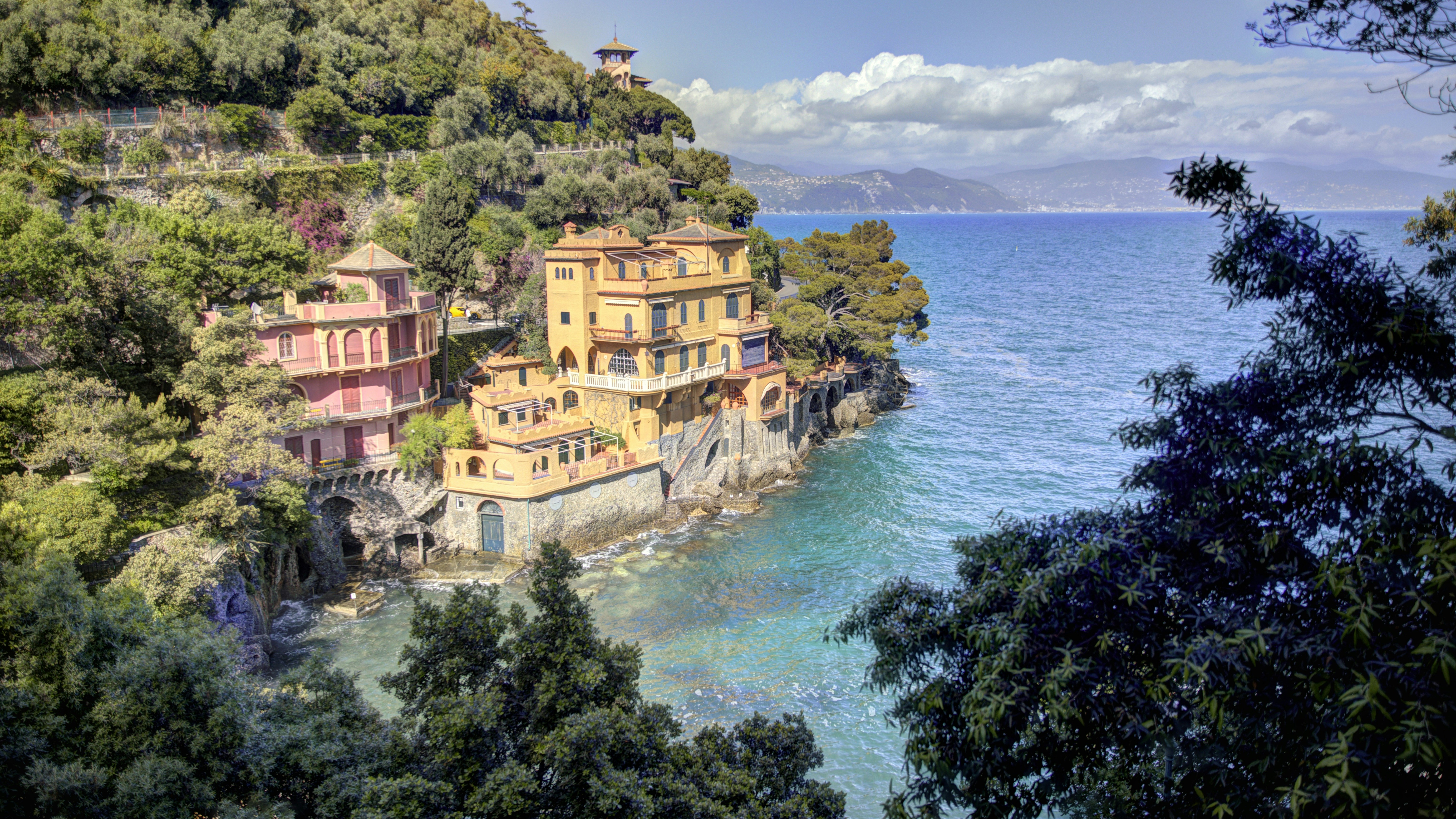 Colorful buildings on a lush cliffside overlooking the blue ocean.