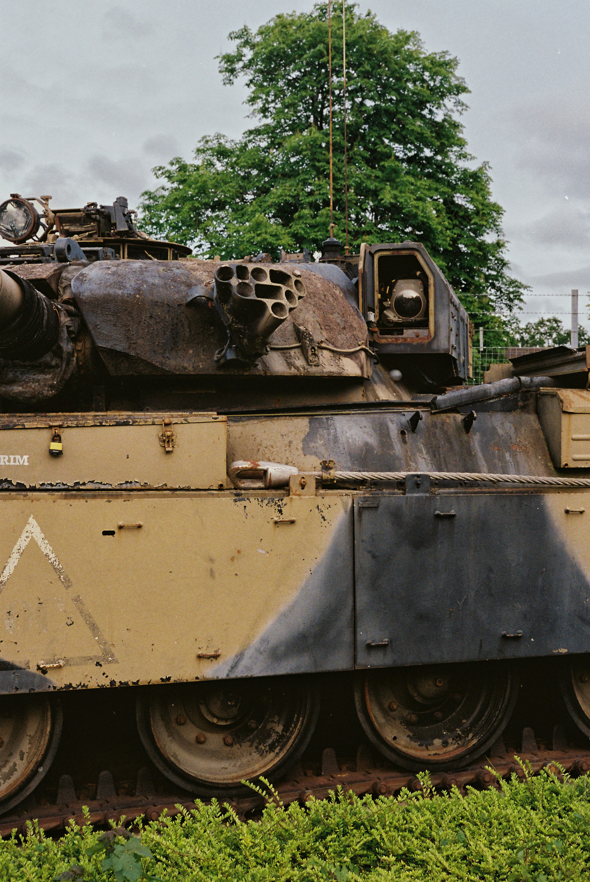 Tanque militar oxidado con patrón de camuflaje y follaje verde.