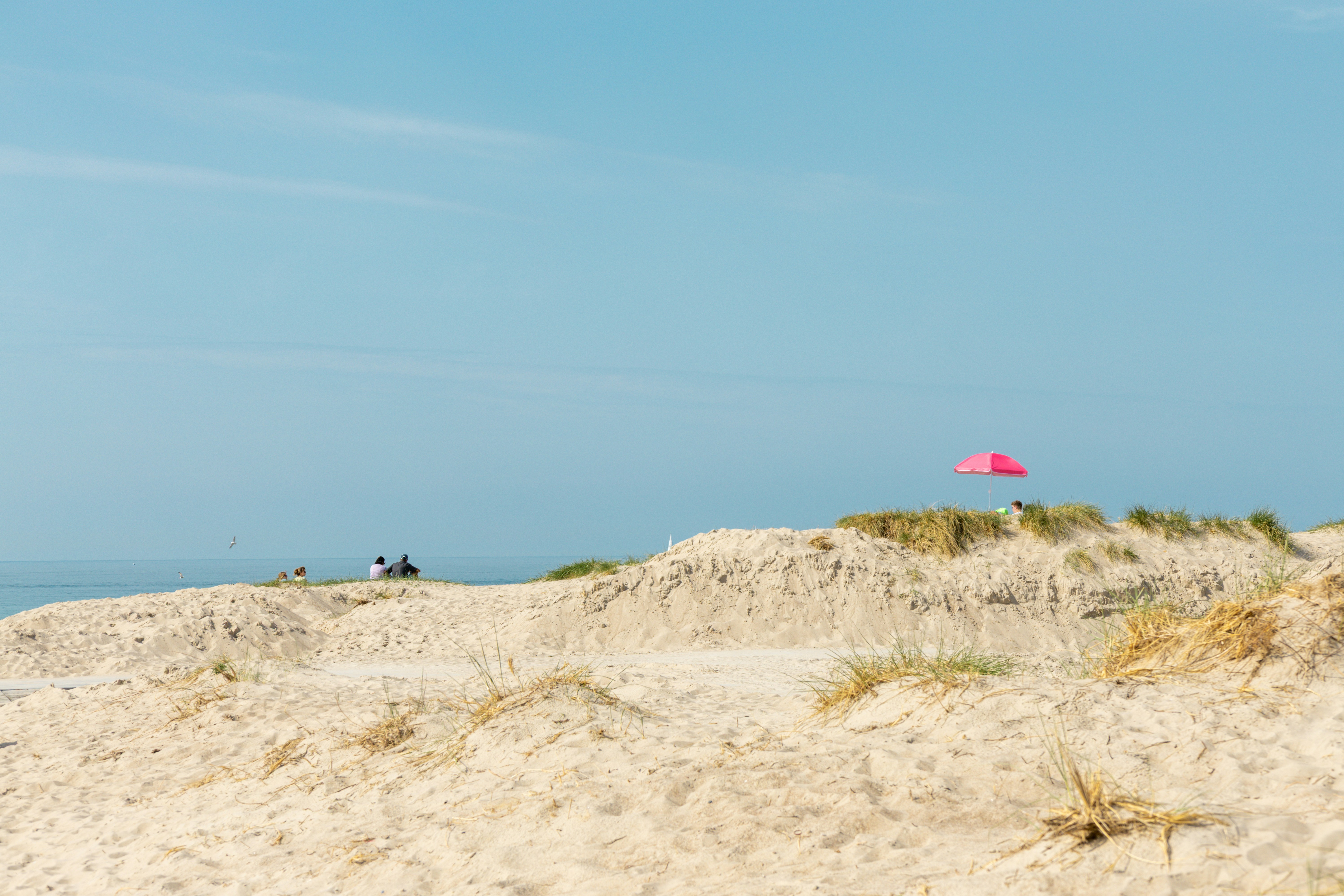 Sand dunes with a pink umbrella and blue sky.