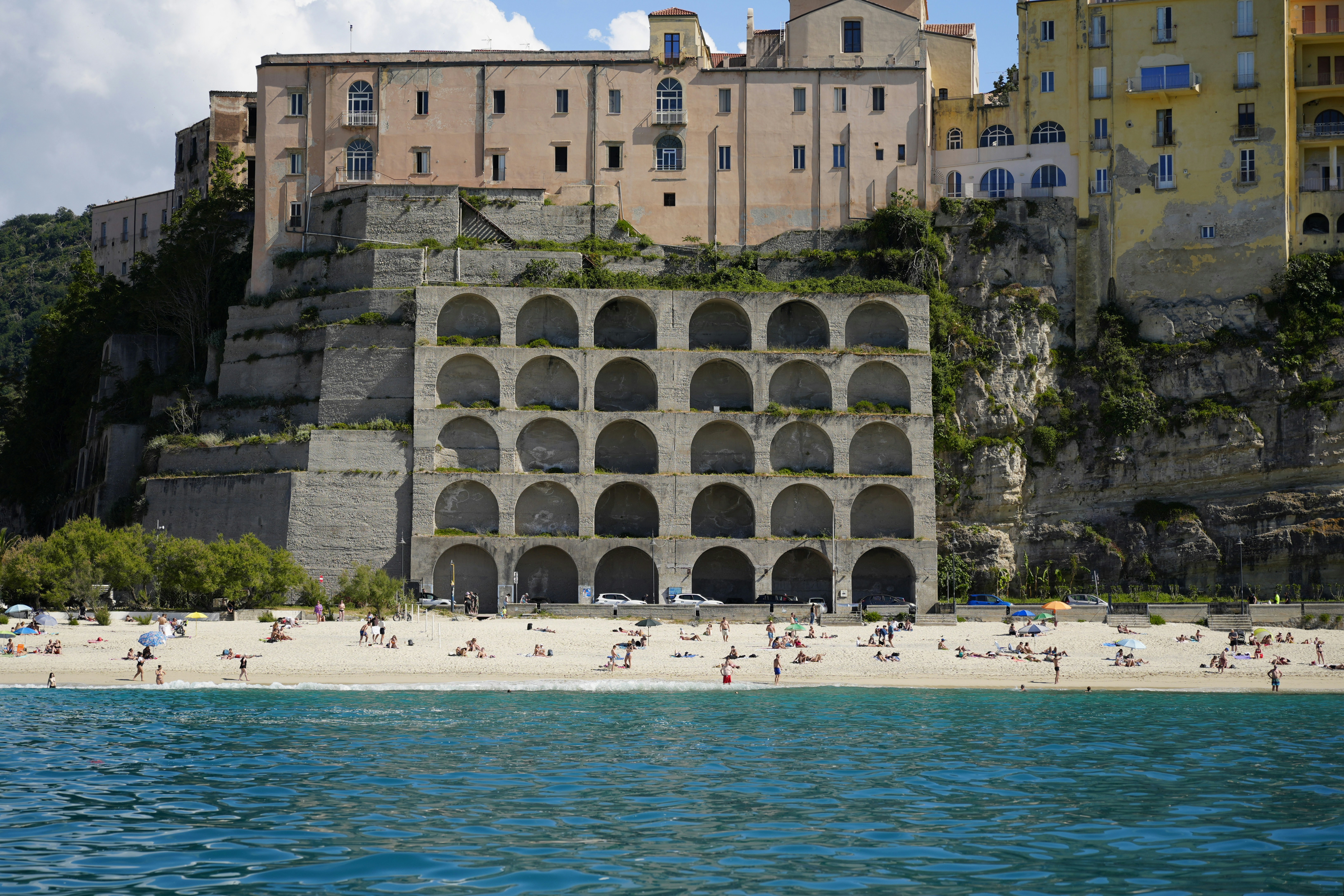 People relaxing on a beach below a cliffside town