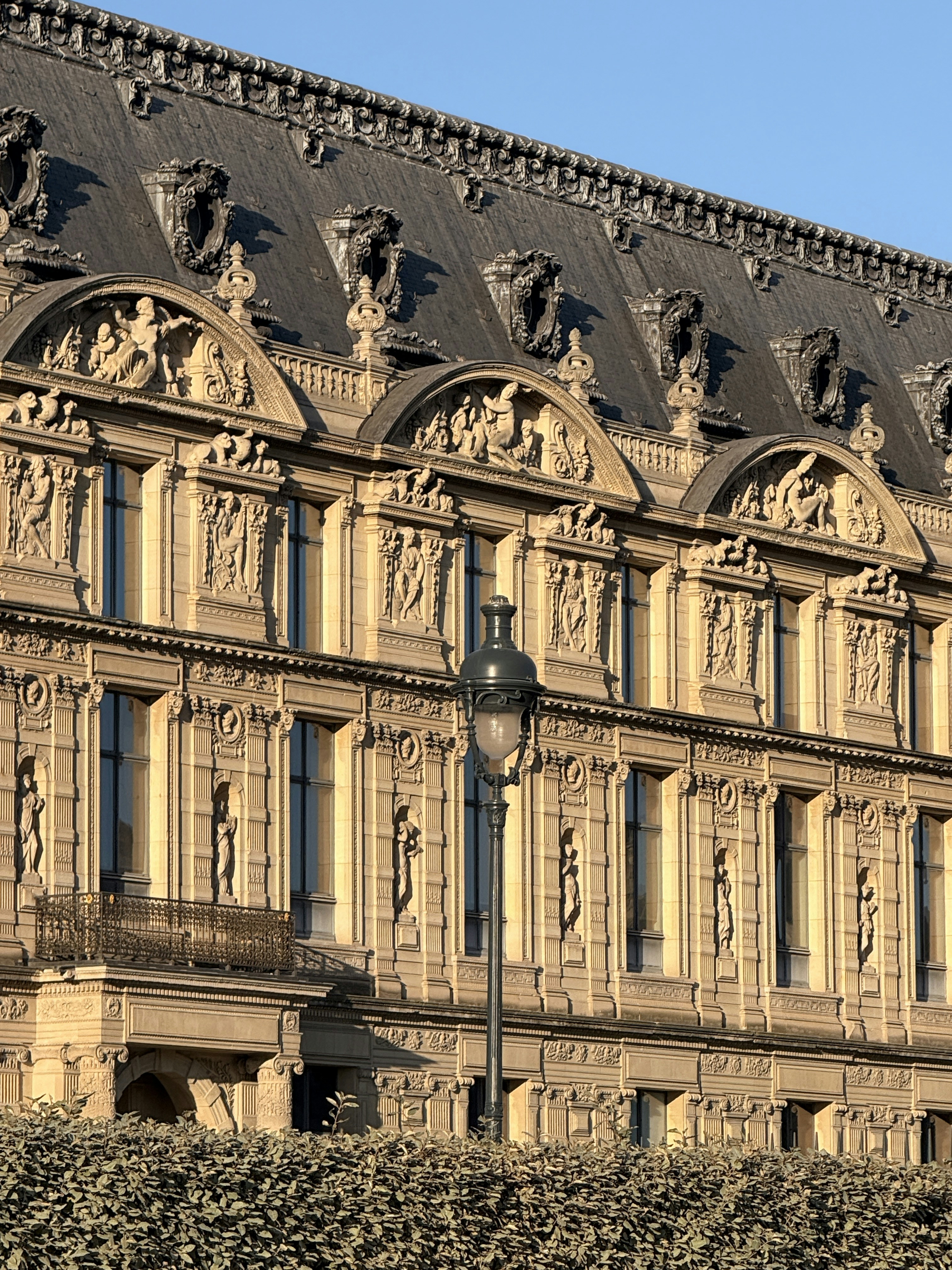 Fachada histórica ornamentada con farola y setos.