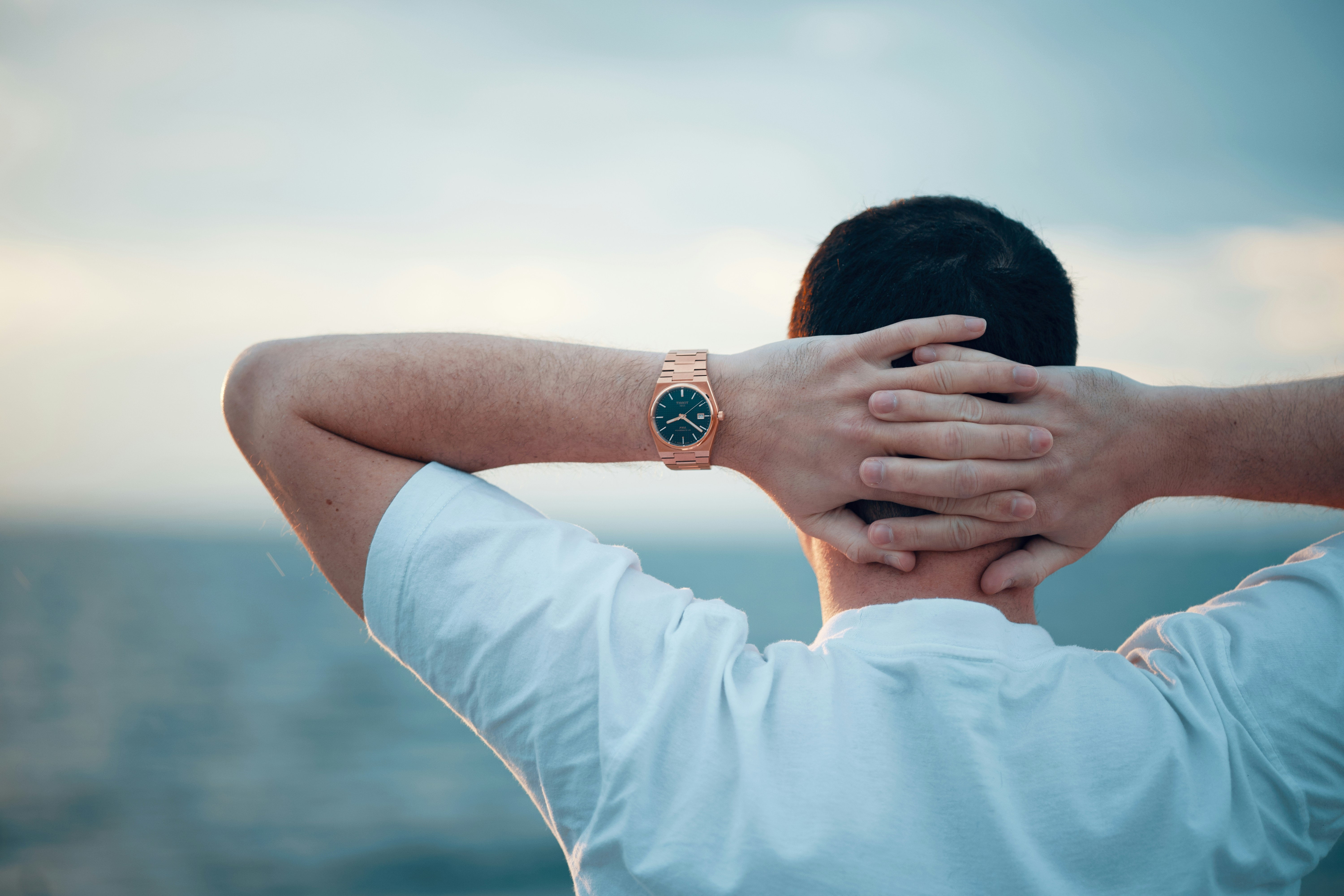 Hombre relajado con las manos detrás de la cabeza, mirando el mar.