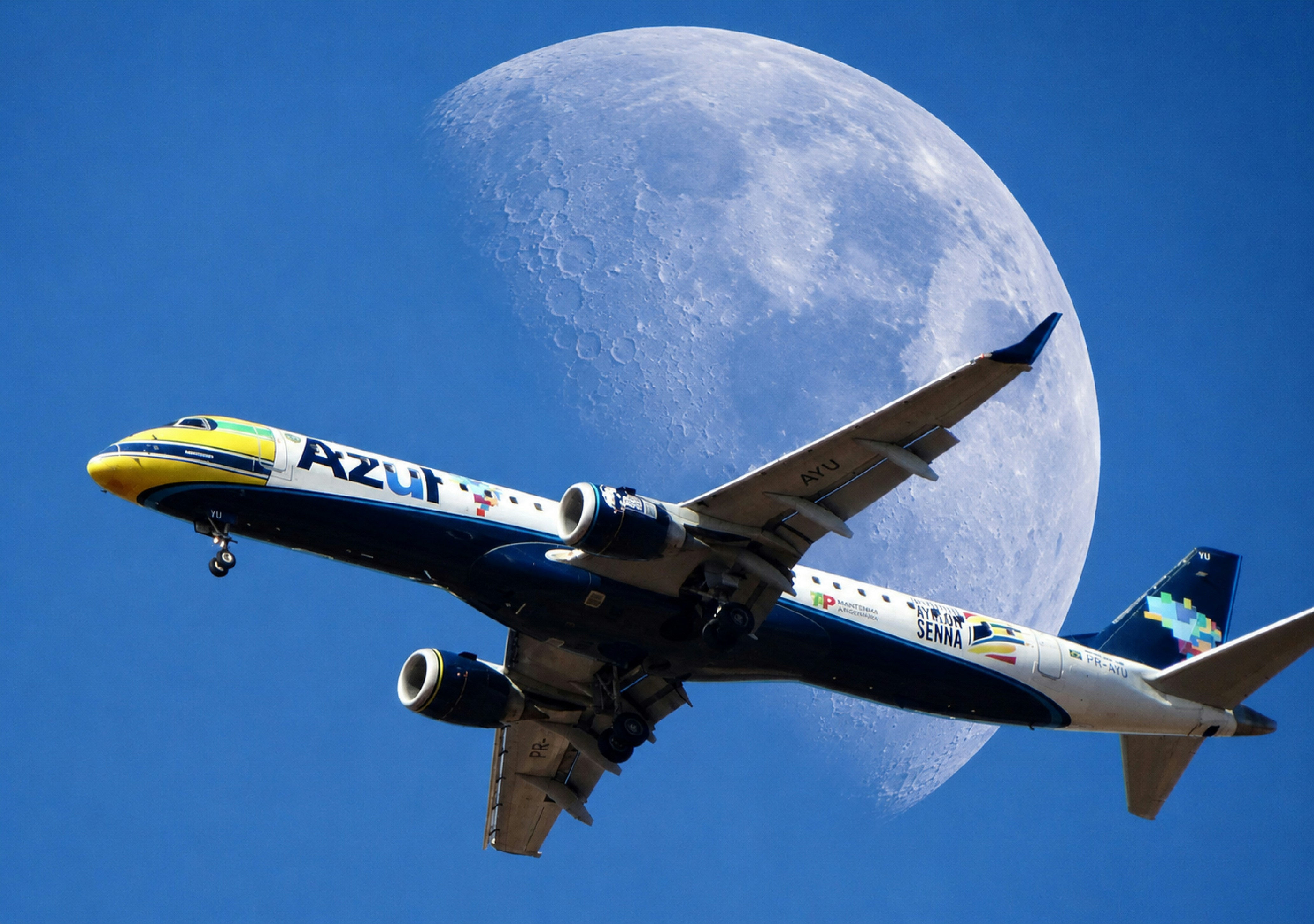 Airplane flying past a large moon in blue sky.