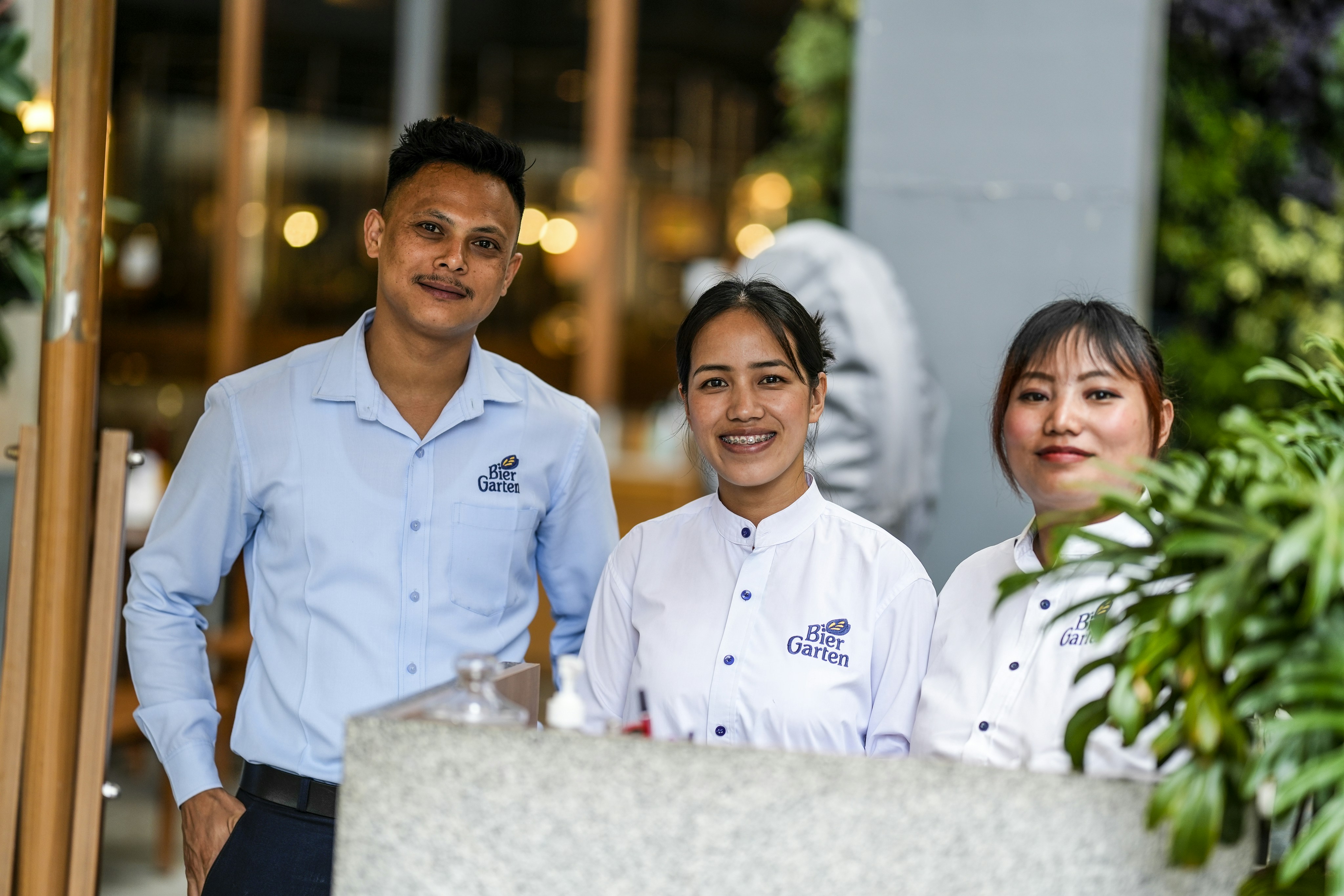 Tiga anggota staf restoran yang tersenyum berdiri di belakang konter.