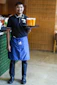 A smiling waiter holds a tray with three orange drinks.