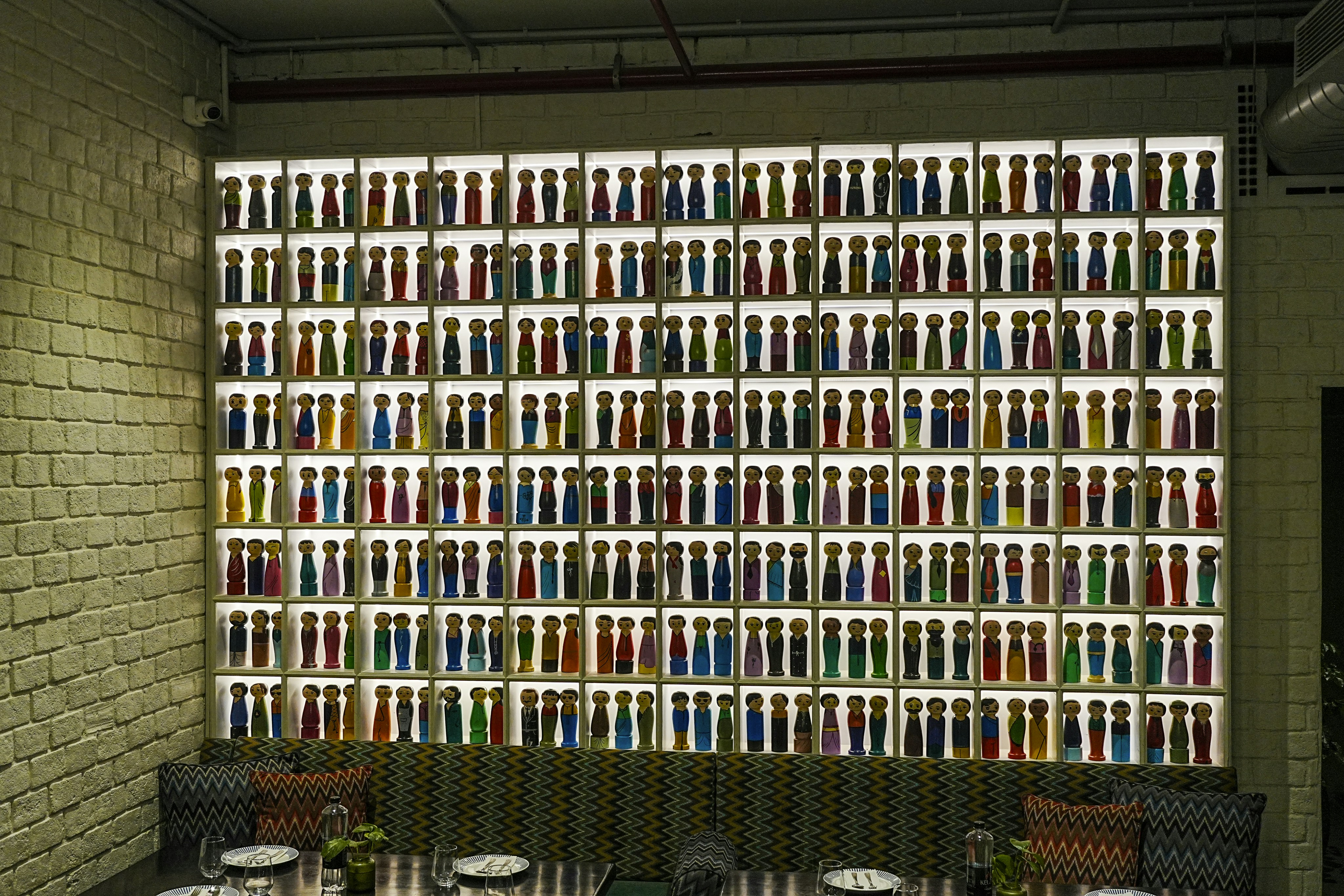 Illuminated wall display with rows of colorful bottles above seating.