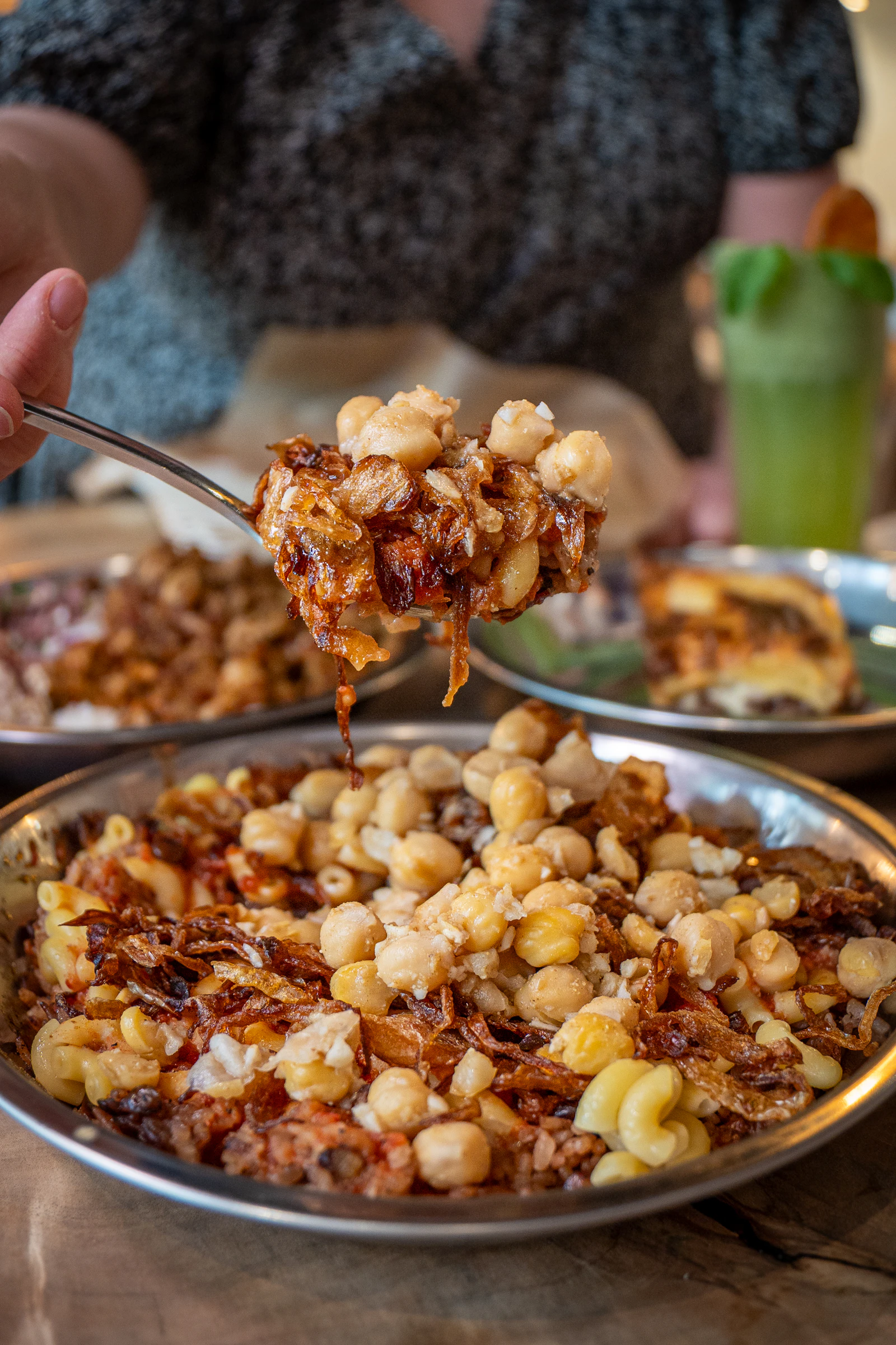 Illustrative image for vegan food in cairo: ful, taameya and koshari: A spoonful of sauced koshary with pasta, chickpeas and fried onions above the bowl.