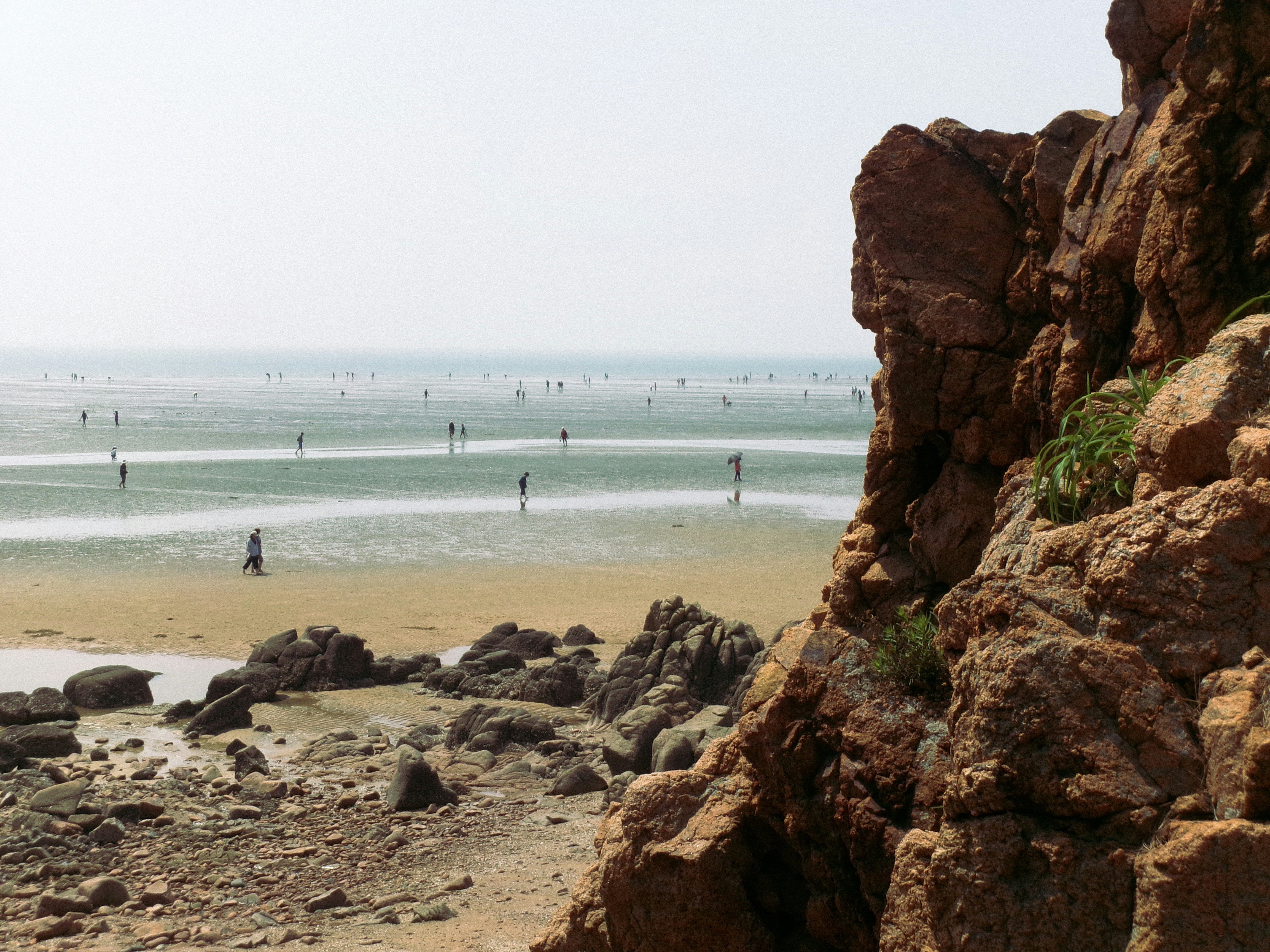 Menschen an einem Sandstrand mit Felsen und flachem Meer.