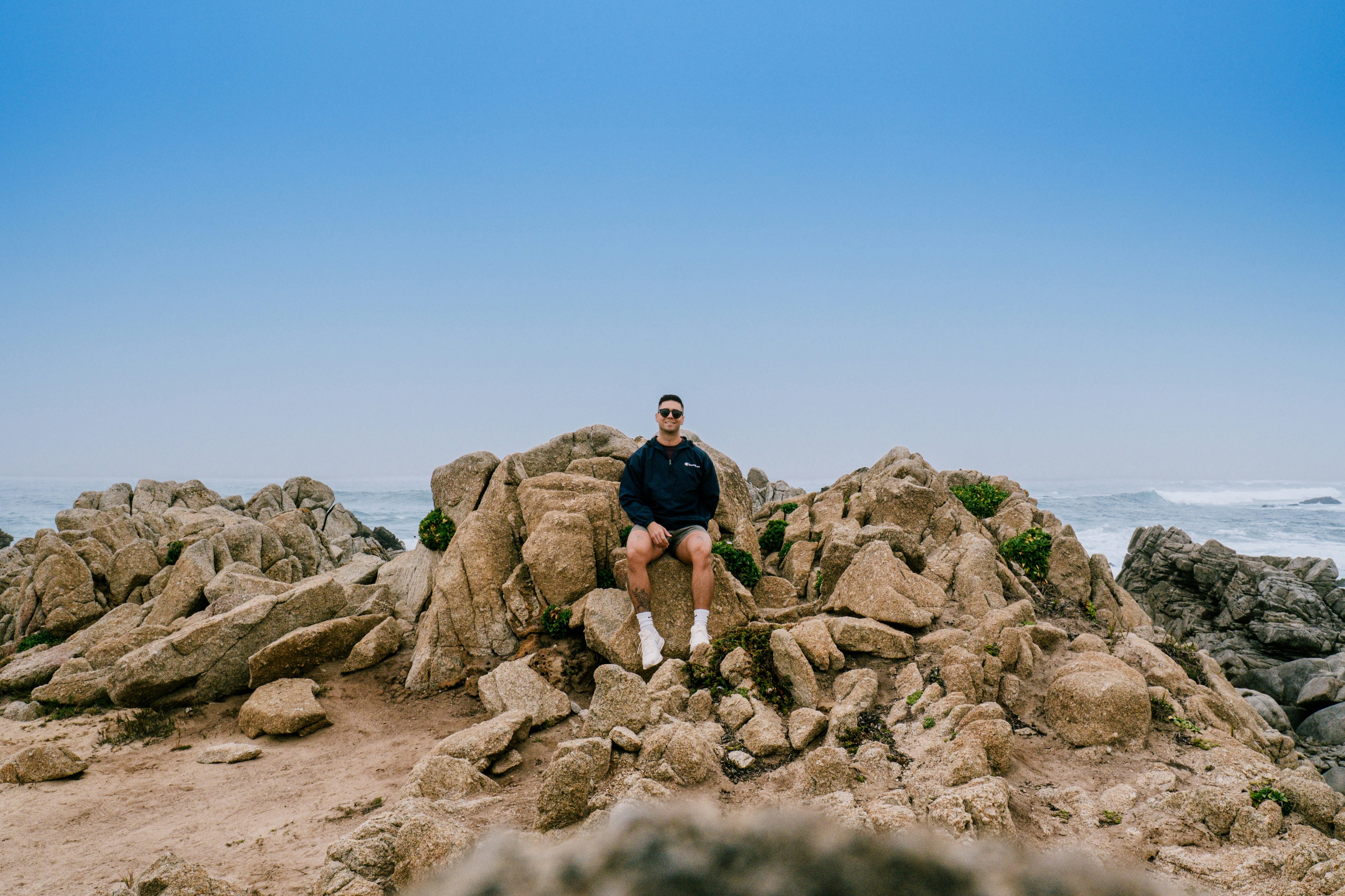 Ein Mann, der auf großen Felsen am Meer sitzt.