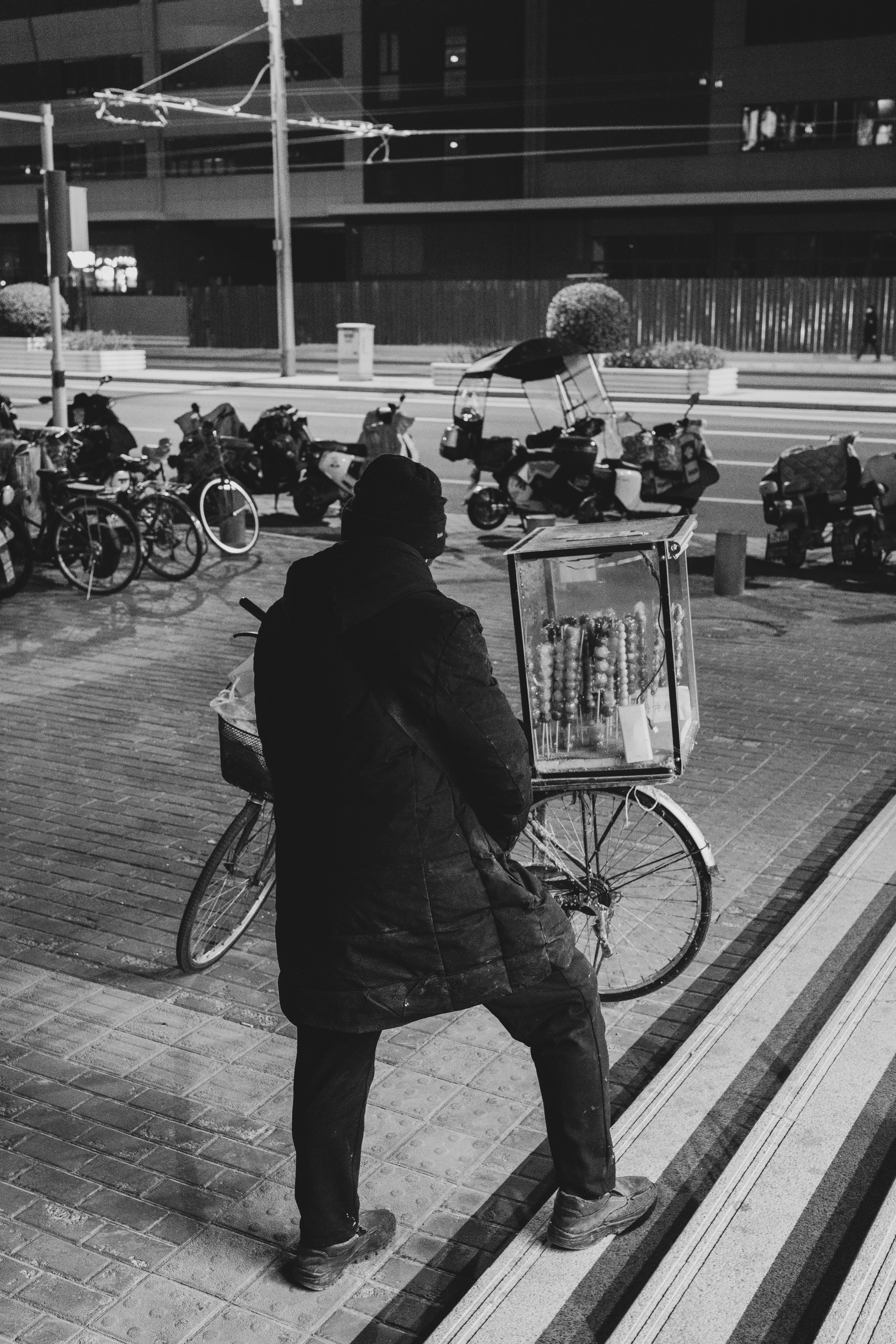 Man stands by bicycle cart on a dark city street