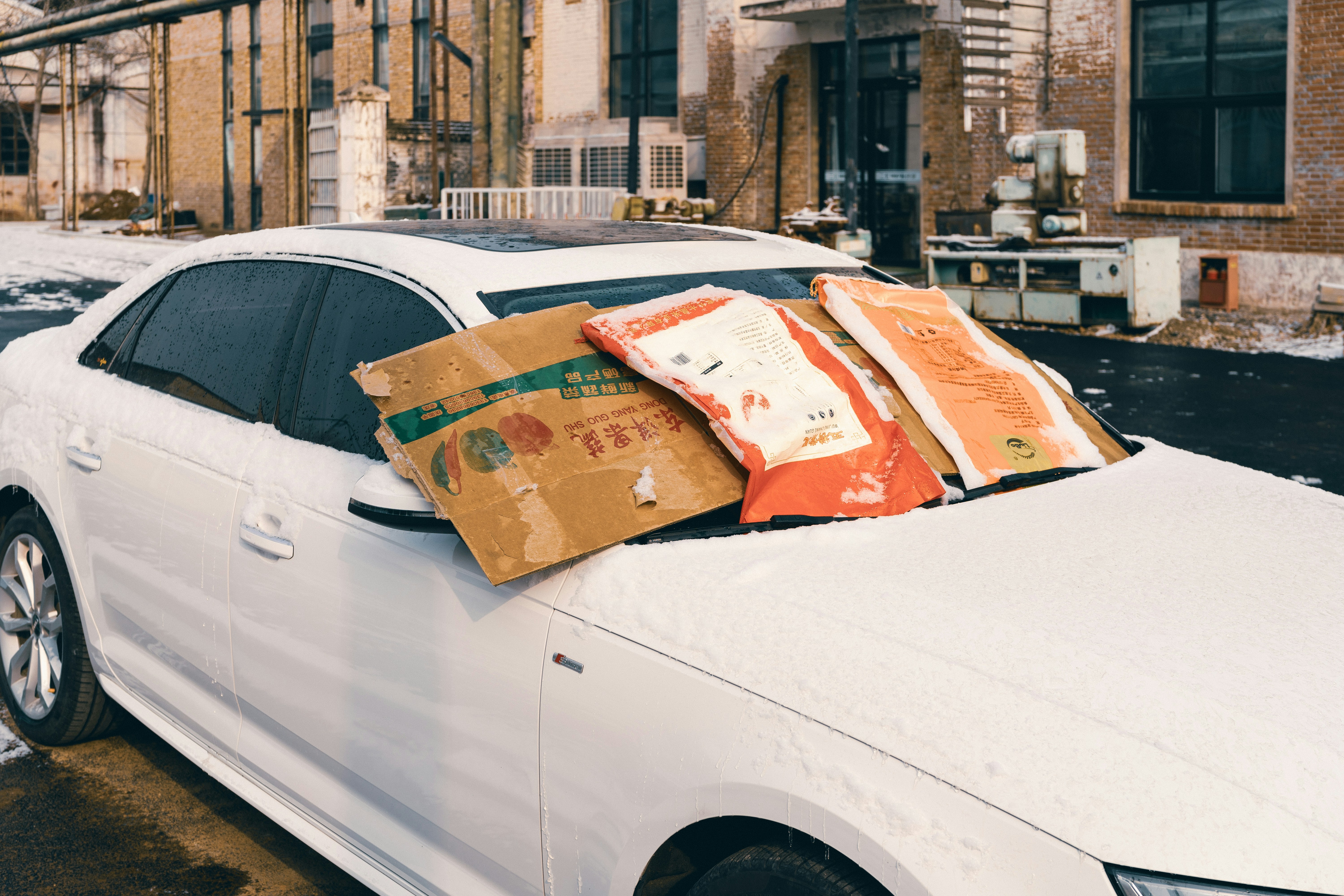 A white car with cardboard and bags covering its windshield.