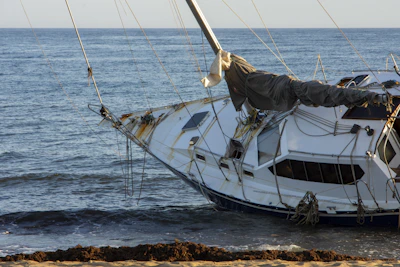 A damaged sailboat washed ashore on a sandy beach.