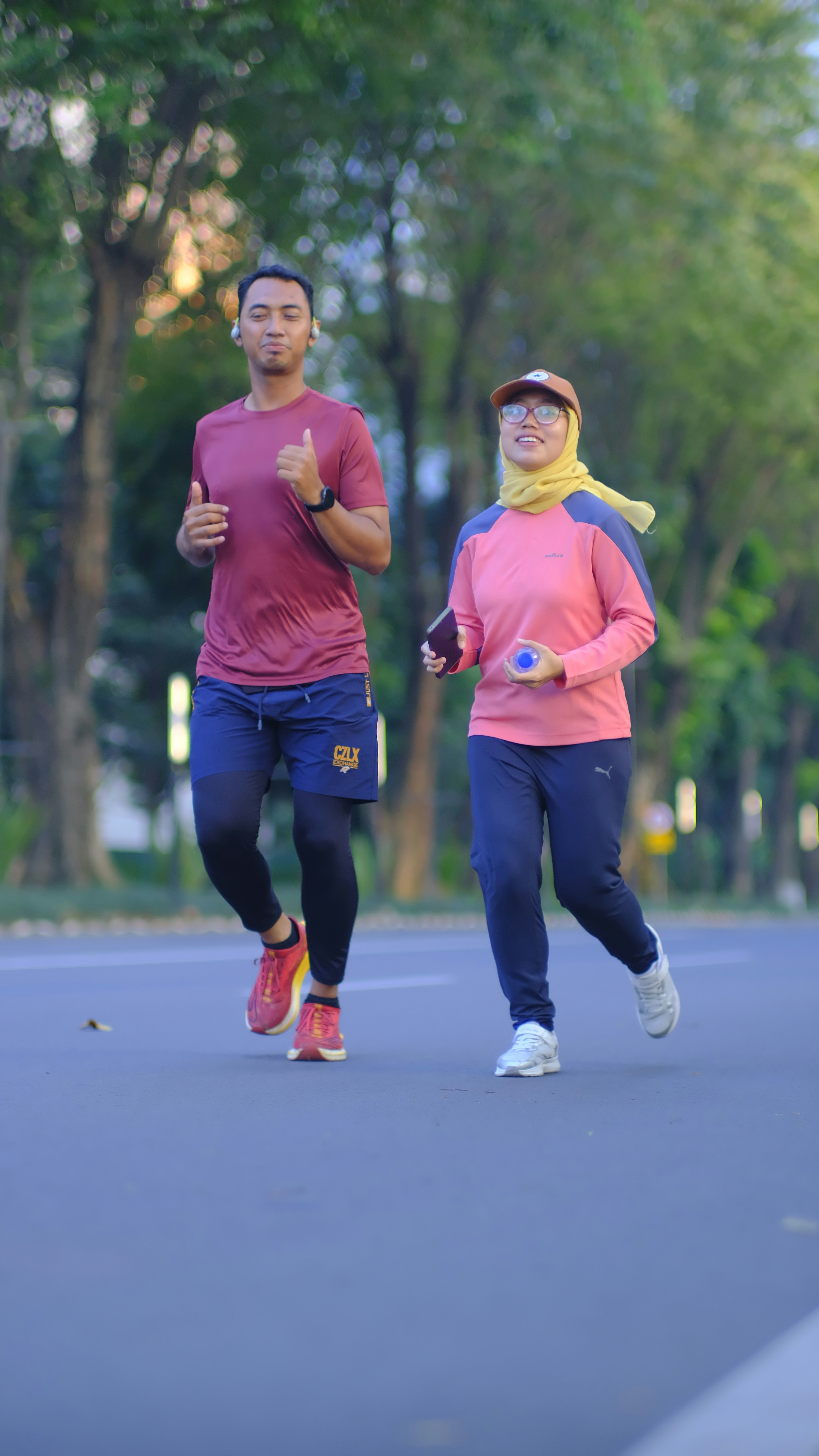 Man and woman jogging together on a tree-lined road.