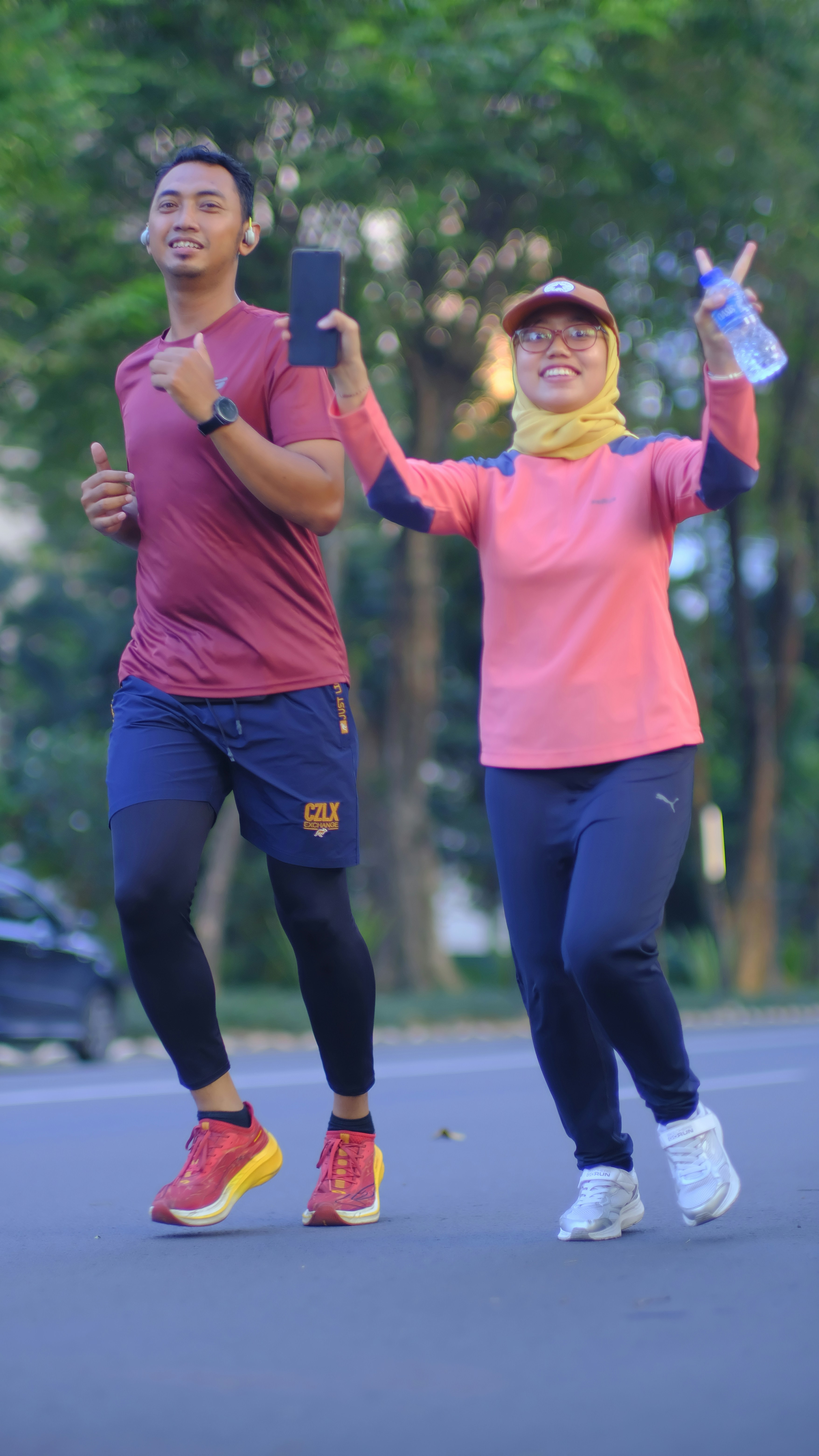 Dua orang bahagia jogging di luar ruangan, wanita memegang air dan telepon.