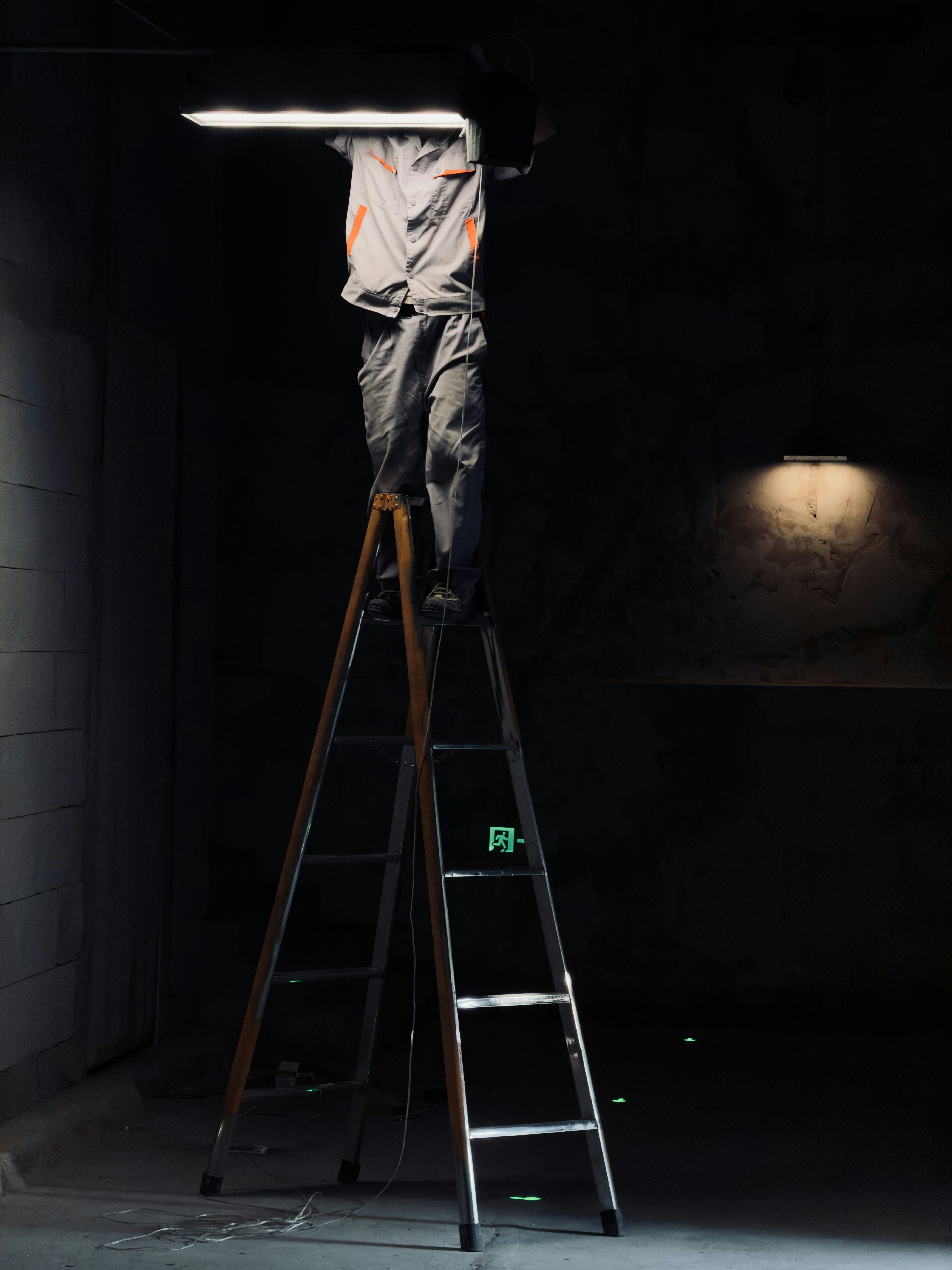 Seorang pekerja di tangga tinggi memasang lampu panjang.