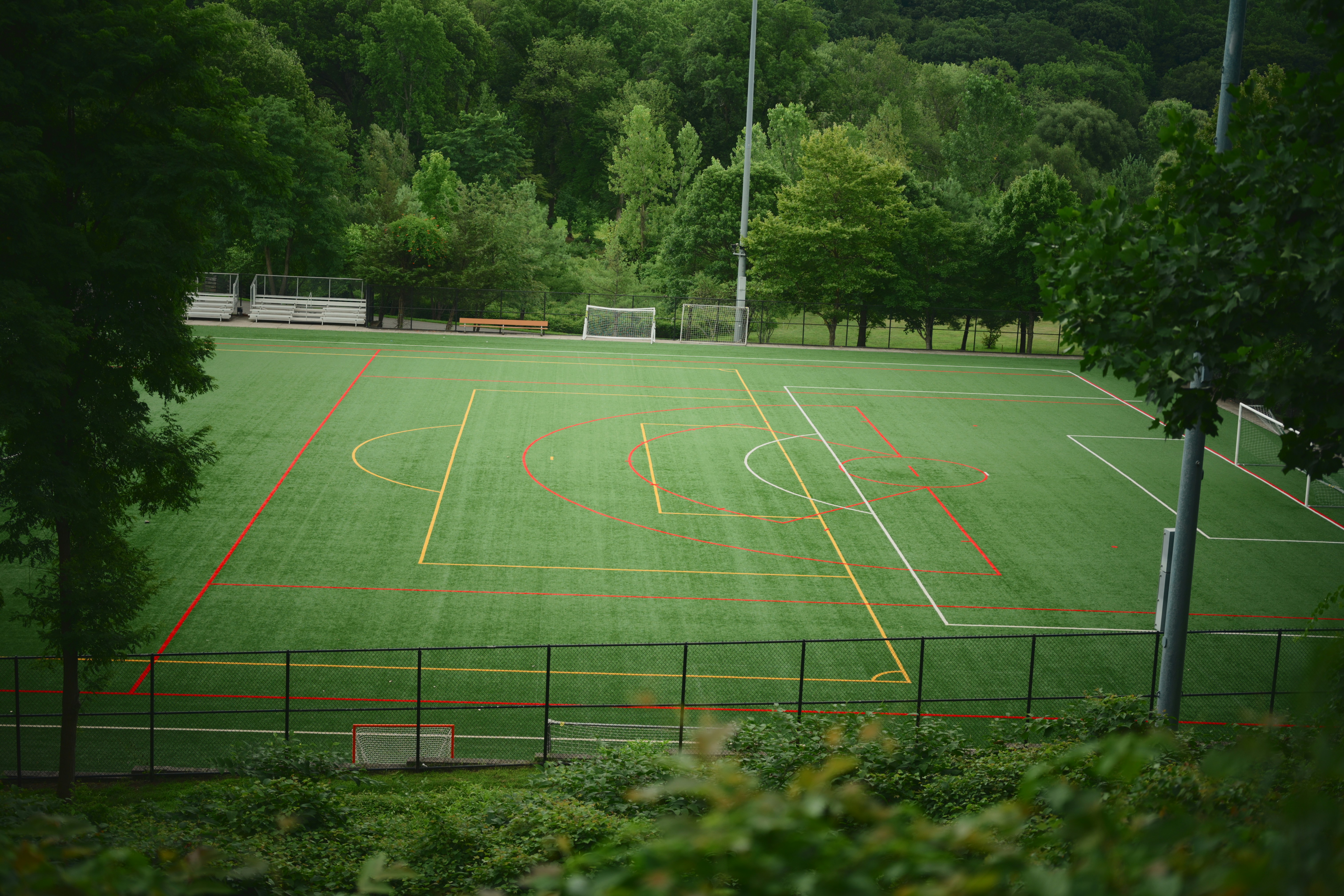 Un terrain de sport en gazon synthétique vert vide entouré d’arbres.