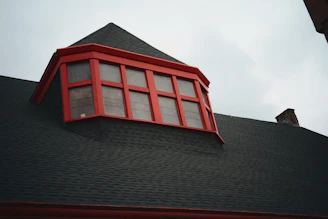 A dark shingled roof with a bright red dormer window.