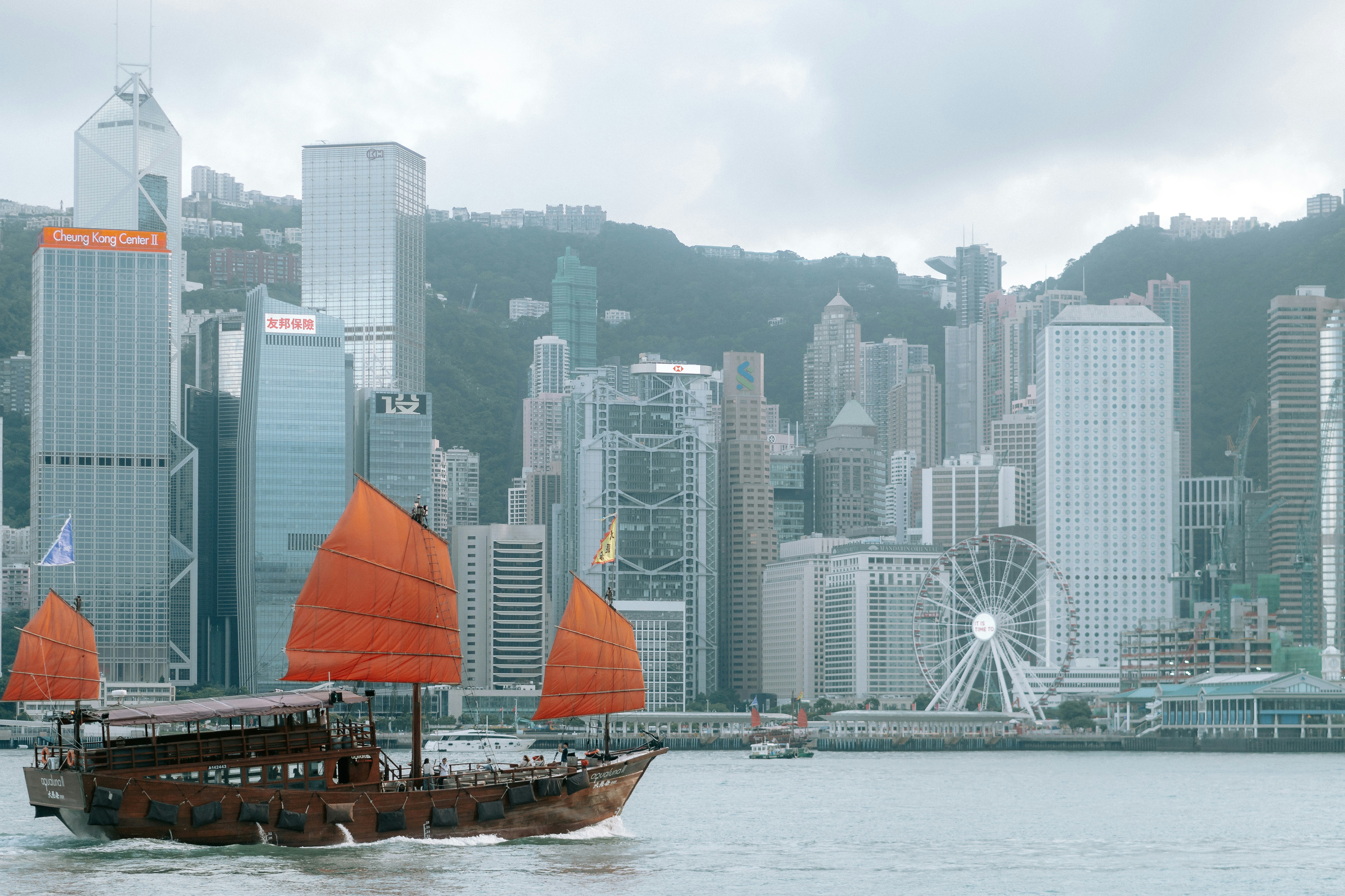 Red-sailed traditional boat sailing past hong kong city skyline.