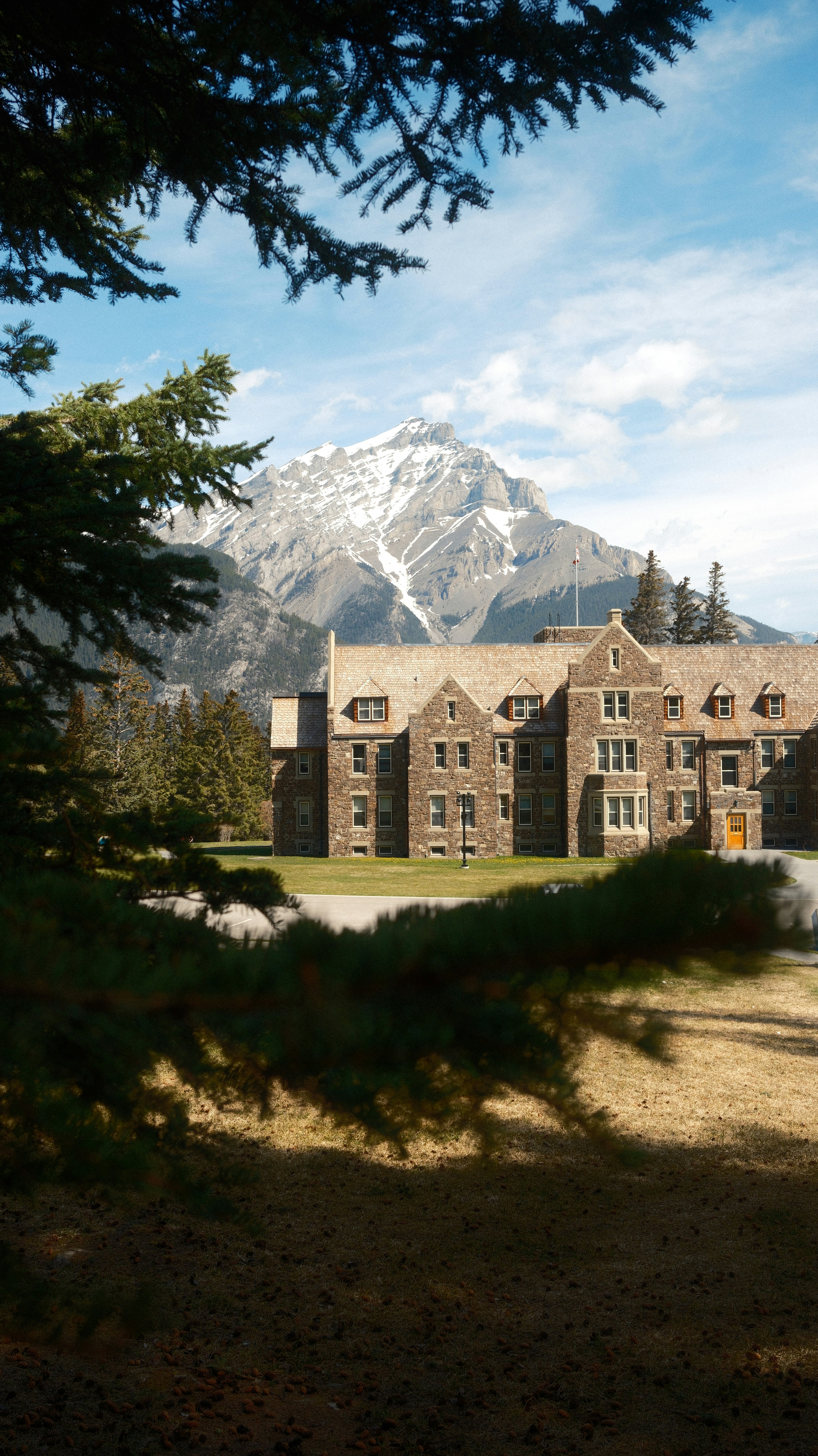 Historic stone lodge framed by pine trees and mountains.