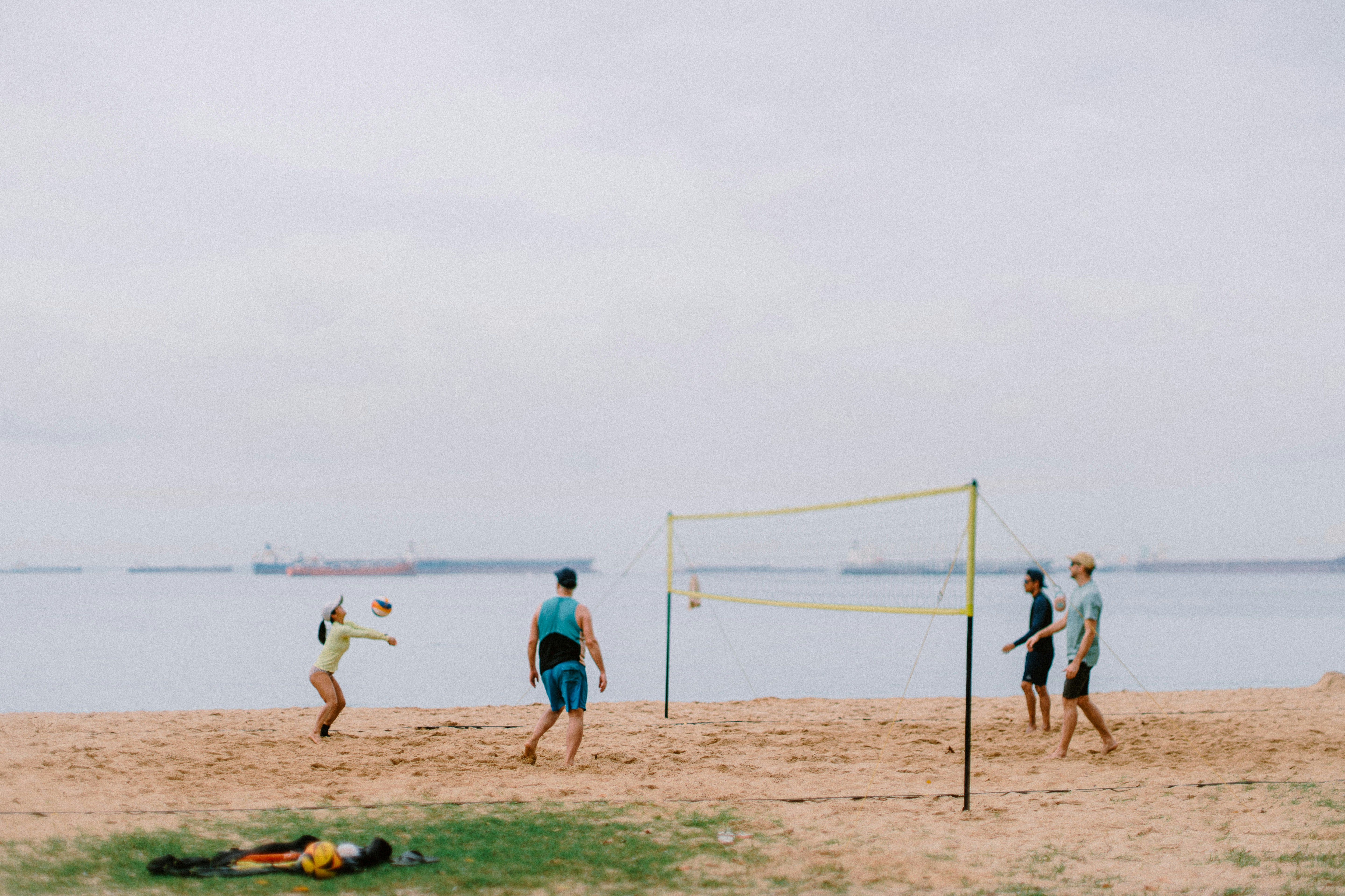 Four people playing beach volleyball by the ocean.